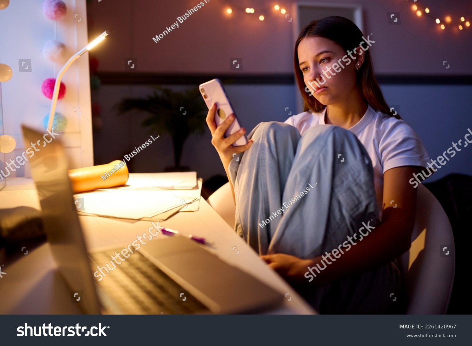 Worried Teenage Girl Sitting At Desk In Bedroom At Home Looking At Mobile Phone At Night #2261420967