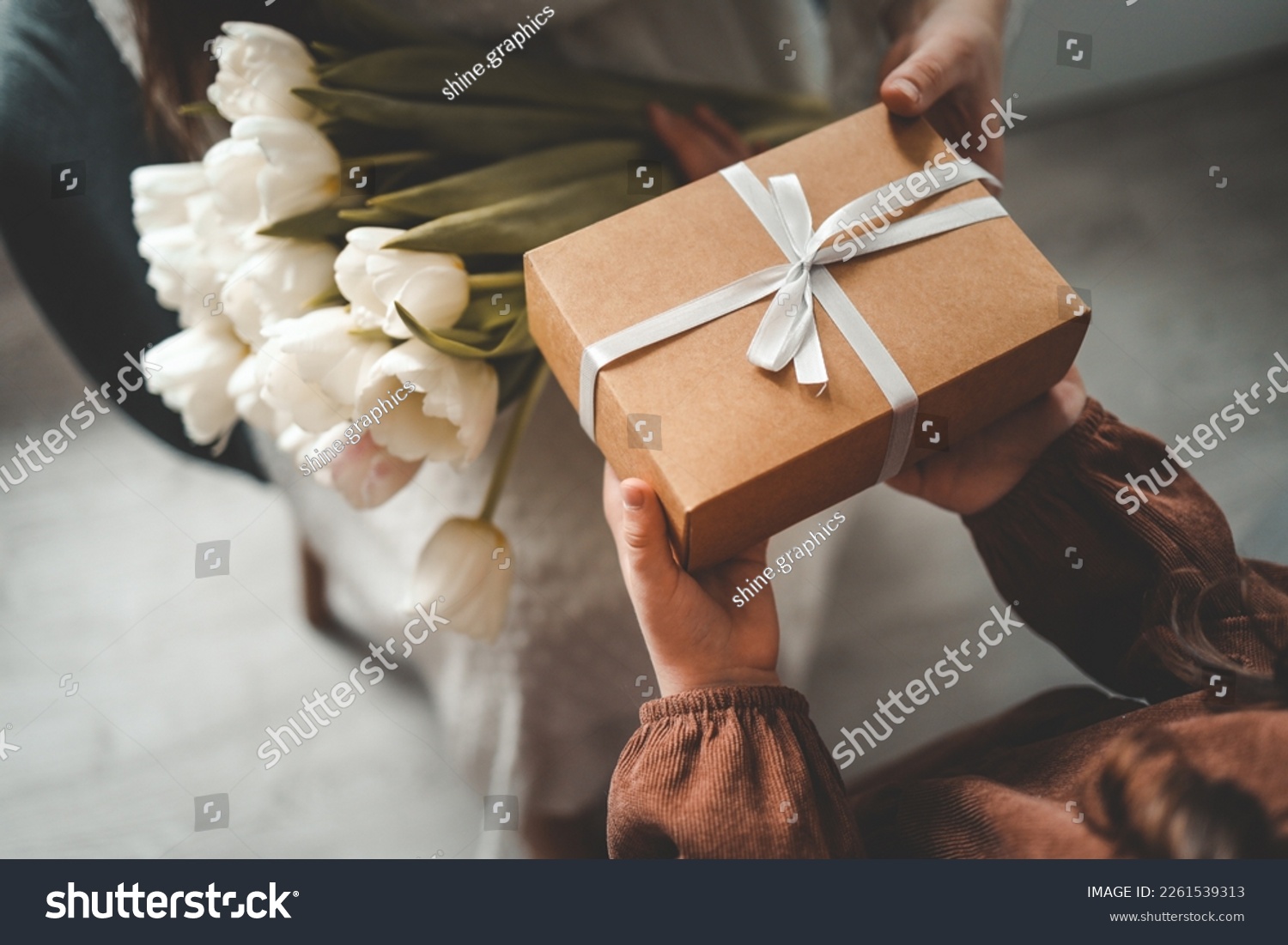 The child's hands hold a beautiful gift box with a ribbon and white tulips. Top view, close-up. Happy mother's day. #2261539313