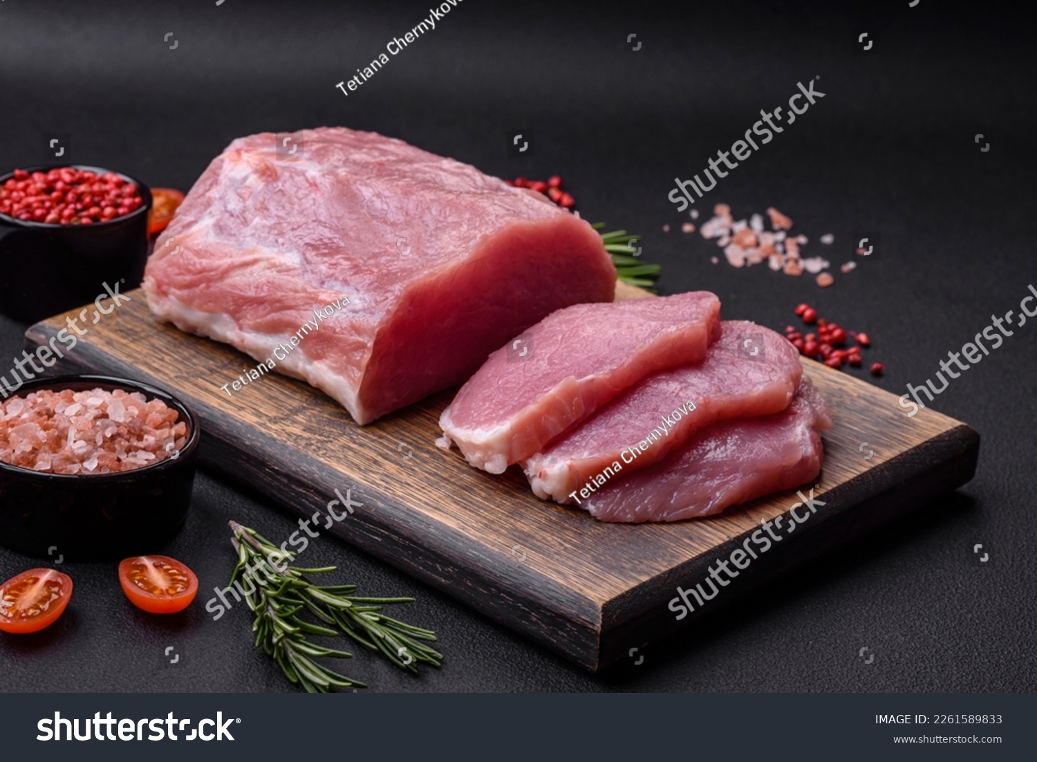 A piece of raw fresh pork on a wooden cutting board with spices and herbs on a dark concrete background #2261589833