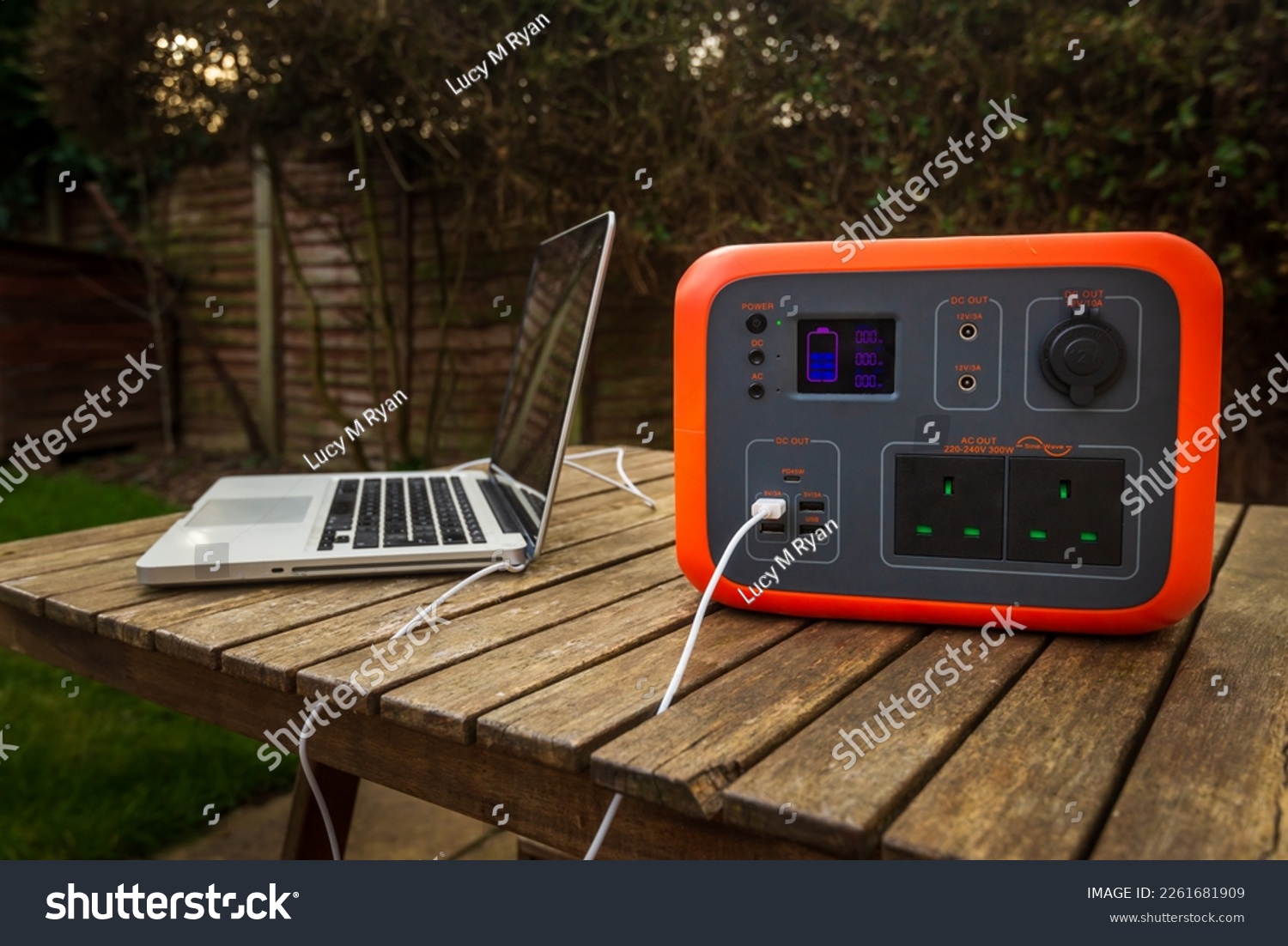 Portable power station solar electricity generator outdoors with laptop plugged in charging. Wireless charging lithium battery backup for power outage emergencies outdoors, camping or travel. #2261681909