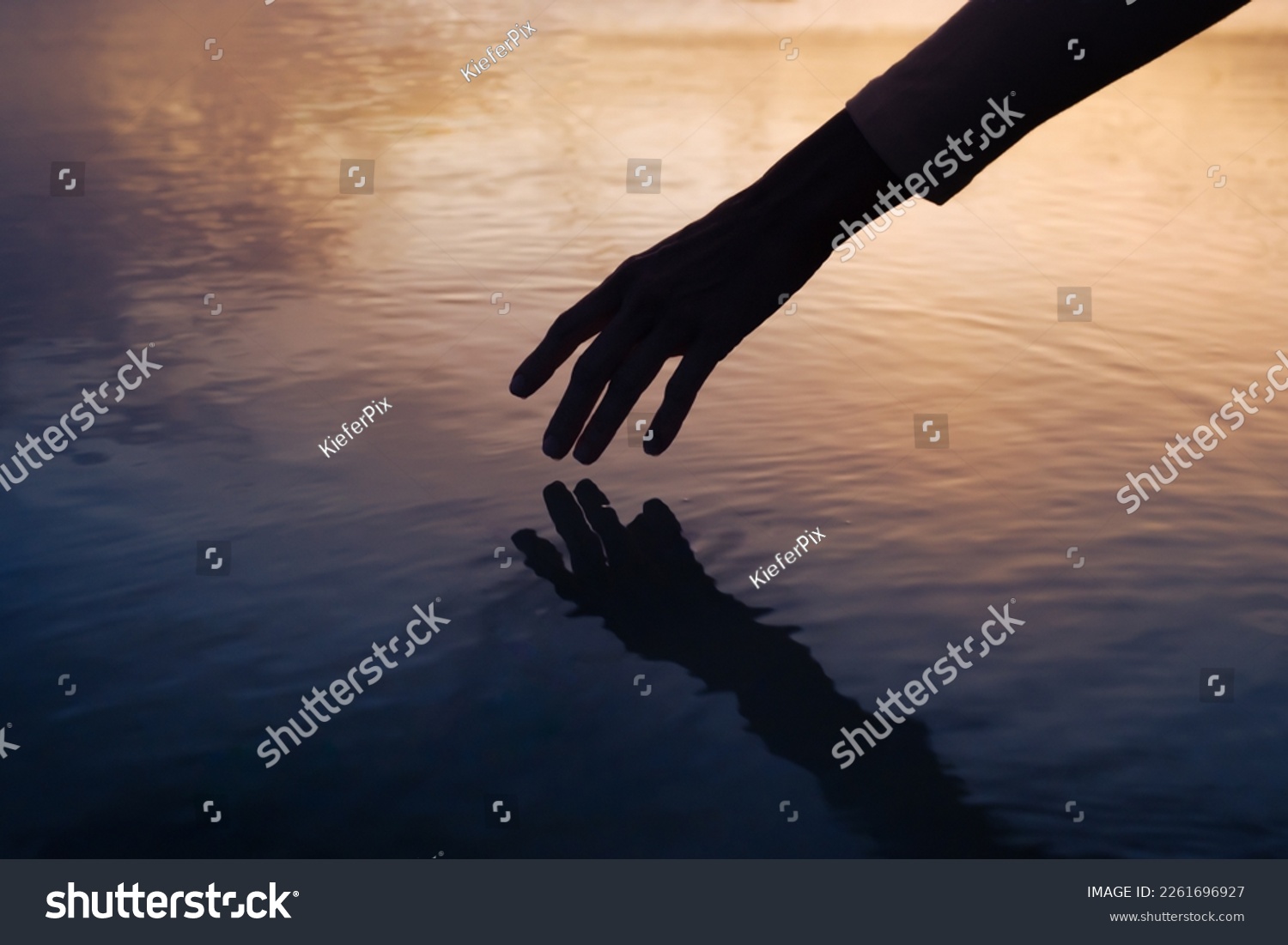 Female hand touching the calm ocean lake water surface reflecting a beautiful colorful summer sunset
 #2261696927