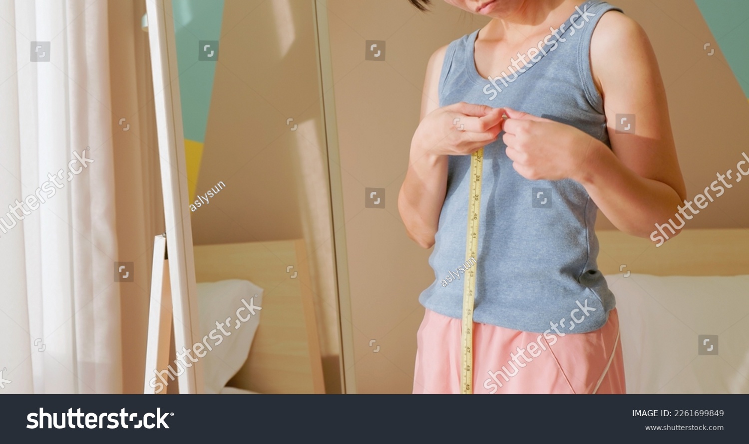 asian unhappy woman is dissatisfied while she measuring her chest and breast in front of mirror #2261699849