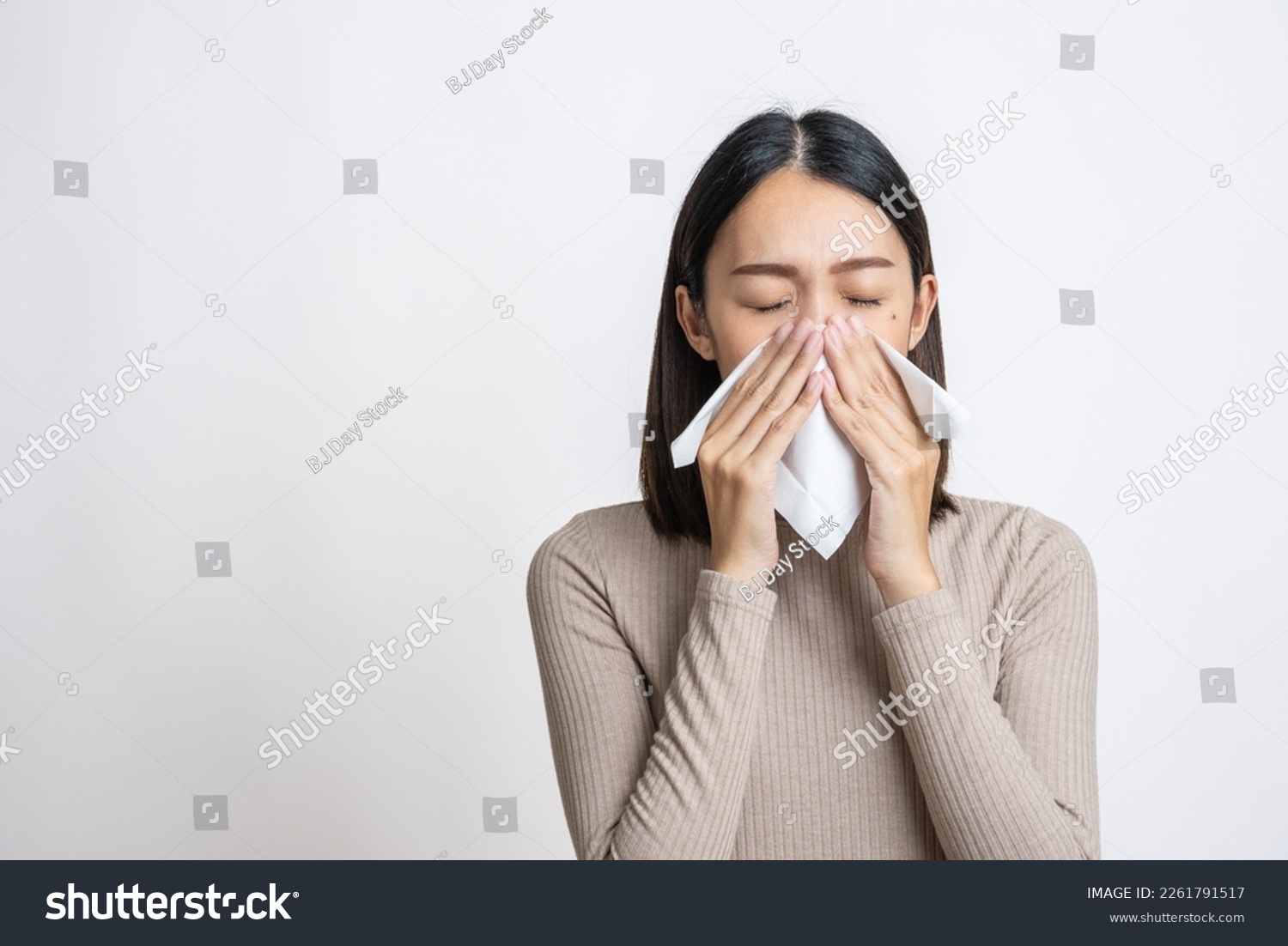 Portrait of beautiful young asian sick woman over isolated white background being wrapped in scarf sneezing, suffering from runny nose and high temperature. Cold and fever concept. #2261791517