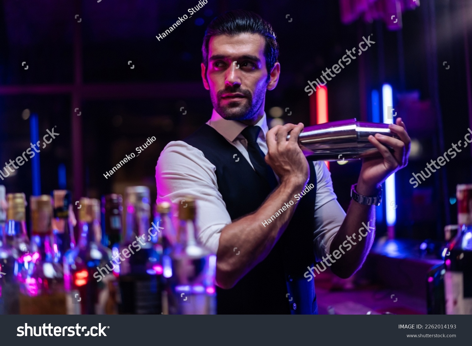 Caucasian profession bartender making a cocktail for women at a bar. Attractive barman pouring mixes liquor ingredients cocktail drink from cocktail shaker into the glass at night club restaurant. #2262014193