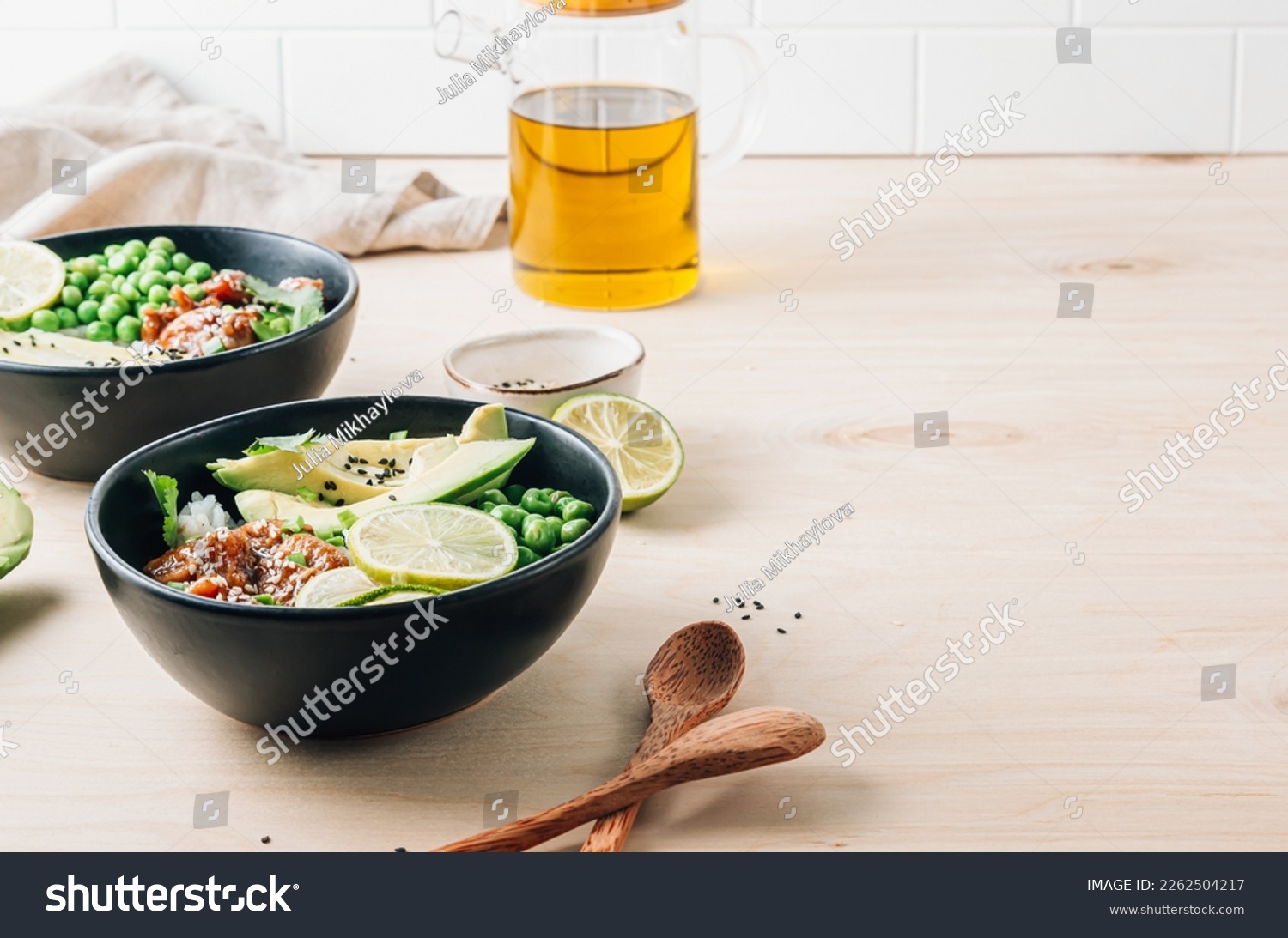 Buddha bowl with crispy sesame chicken. Sweet and sour fried chicken with steamed rice, peas and acocado on light wooden background. Healthy and balanced food concept. Selective focus with copy space #2262504217
