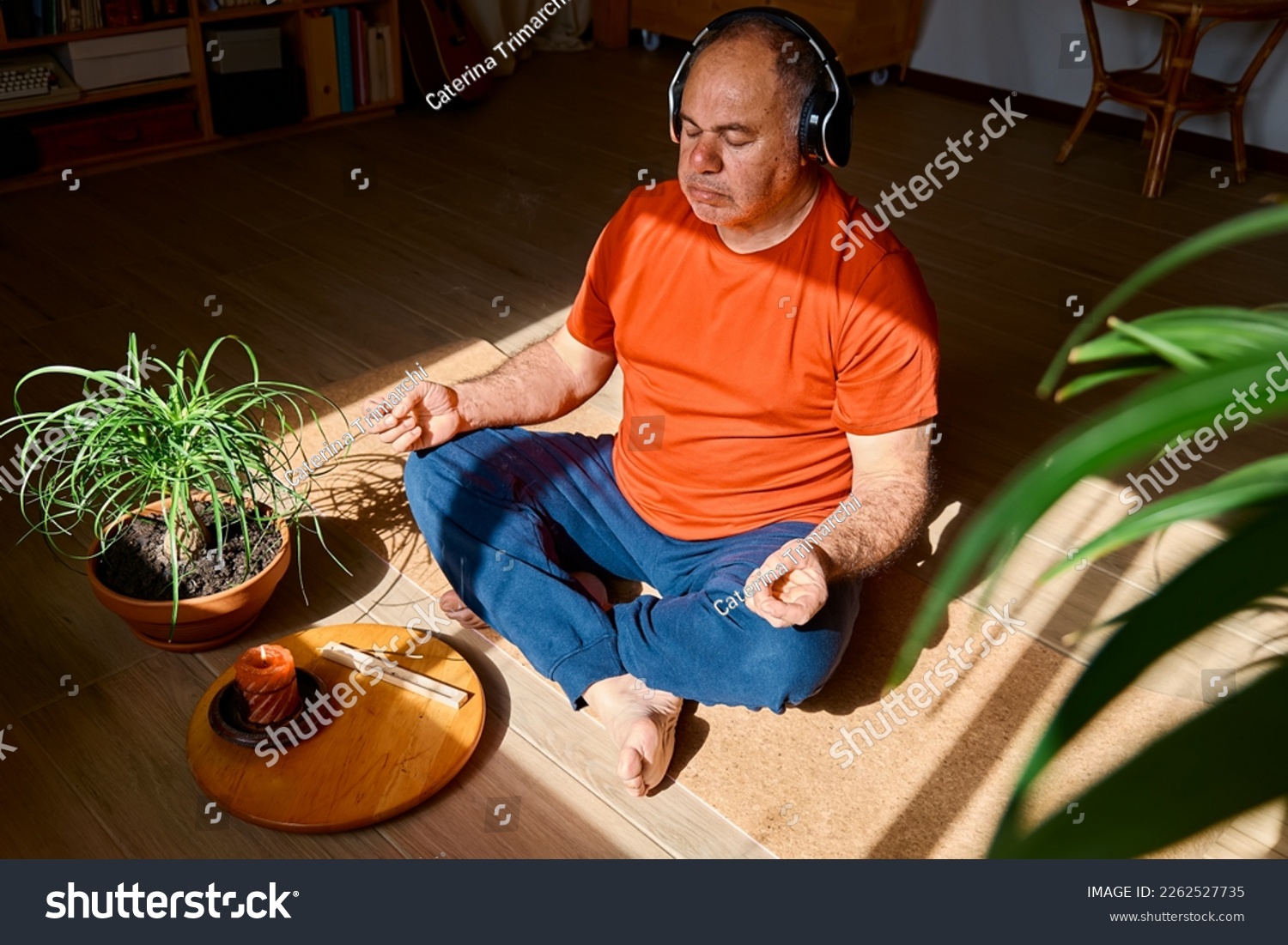 Mature middle-aged overweight man in wireless headphones relaxing at home with guided meditation, listening to relaxing music and meditating in lotus pose. #2262527735