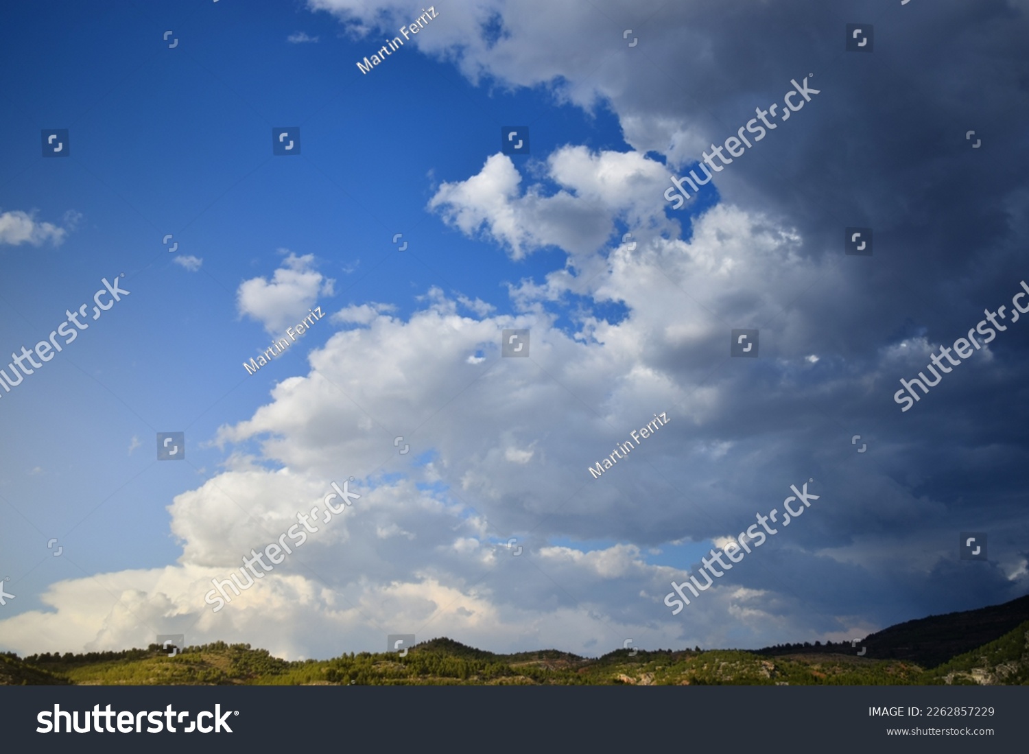 Storm clouds advance on a clear blue sky over a narrow mountainous horizon #2262857229