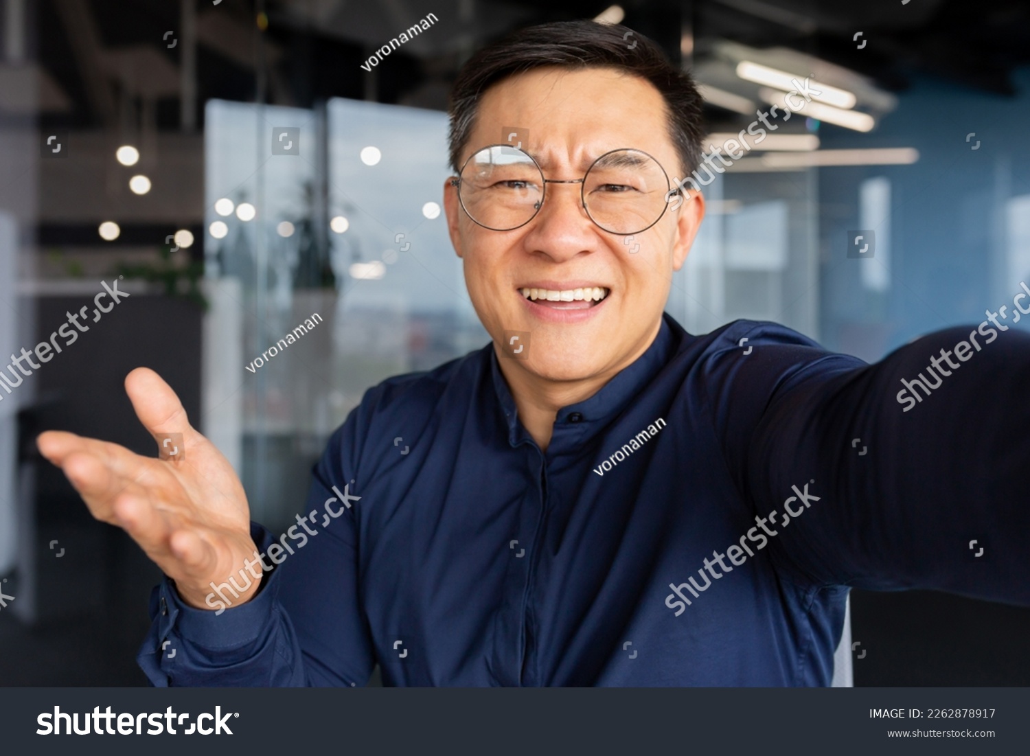 Angry and grumpy asian businessman talking on video call, man inside office looking at smartphone camera, boss in casual shirt shouting at camera. #2262878917
