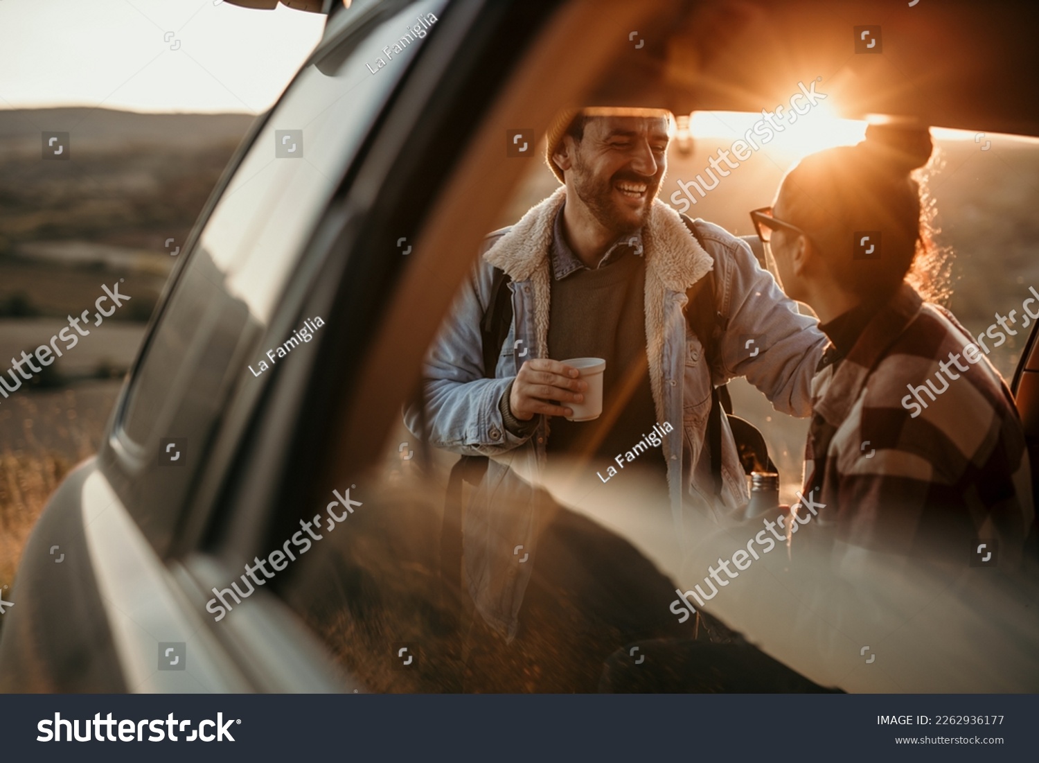 Young couple talking, drinking a coffee watching the sunset from their car. Couple travel concept #2262936177