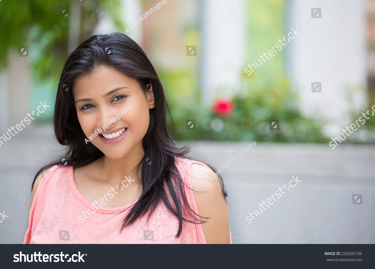 Closeup portrait of confident smiling happy pretty young woman in pink dress, isolated background of blurred trees, flowers. Positive human emotion facial expression feelings, attitude, perception #226305736