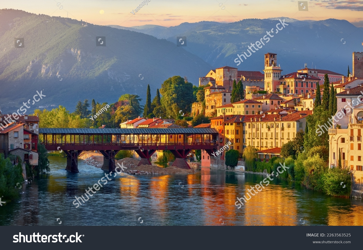 Bassano del Grappa, Veneto, Italy. Bridge Ponte degli Alpini at river Brenta. Panoramic view old town with vintage building tower, wooden Alpine mountains scenic sunset landscape #2263563525