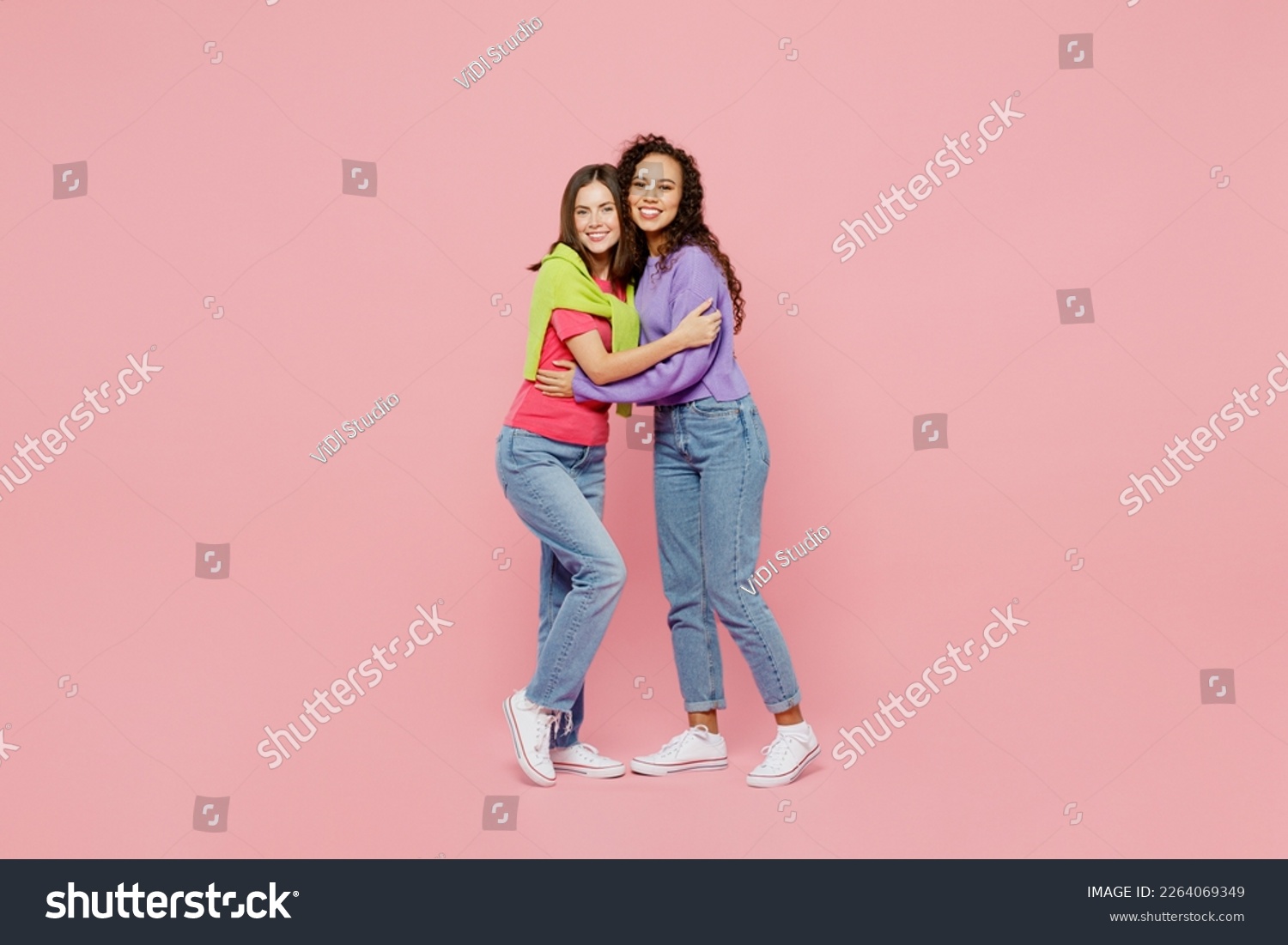 Full body young two friends smiling happy fun cool cheerful positive women 20s wear green purple shirts together stand look camera hug homie isolated on pastel plain light pink color background studio #2264069349