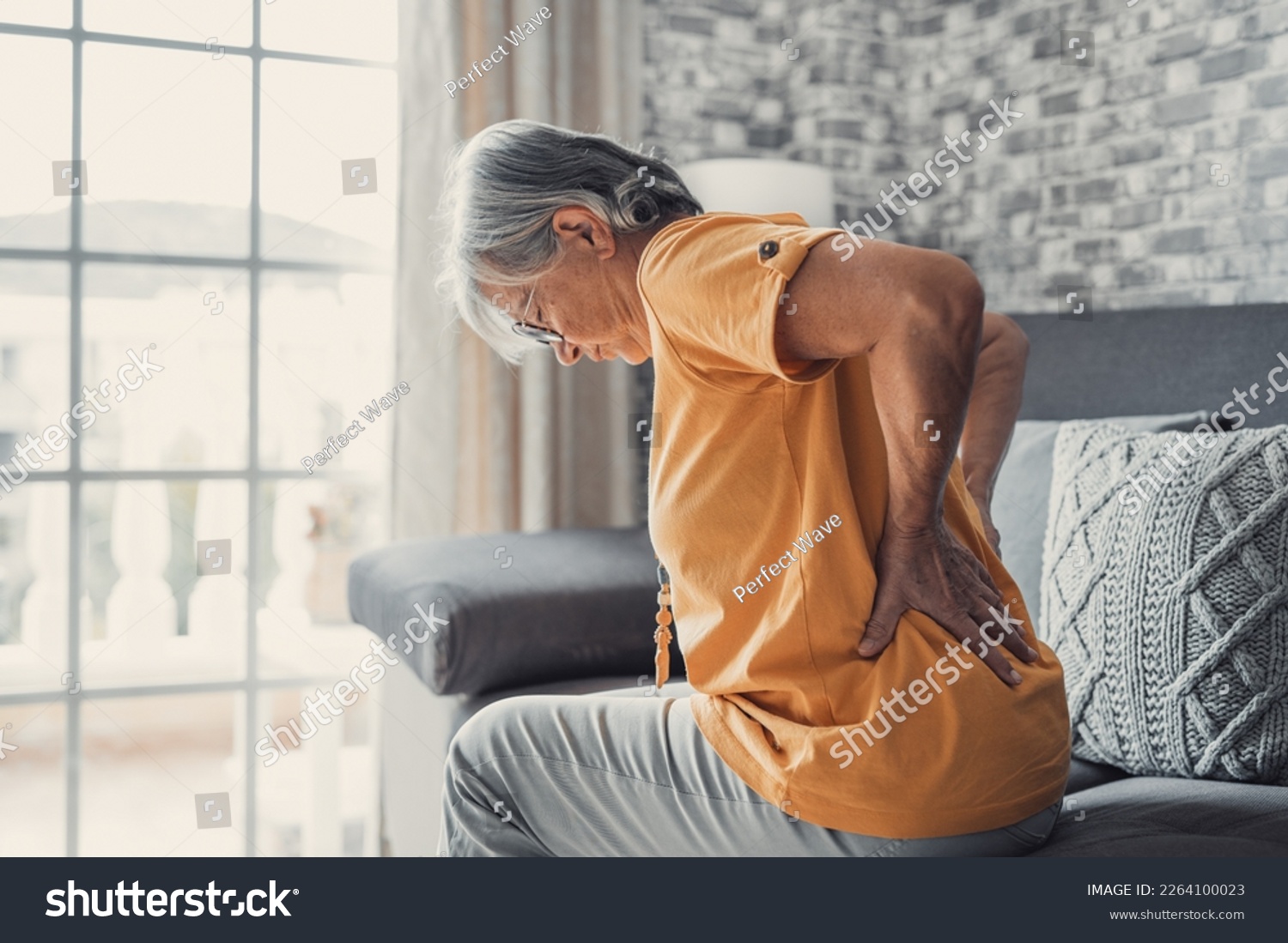 Unhappy mature woman touching back, feeling pain, sitting on couch in living room, unhealthy middle aged senior female suffering from backache, spinal problem, rubbing stiff muscles or kidney #2264100023