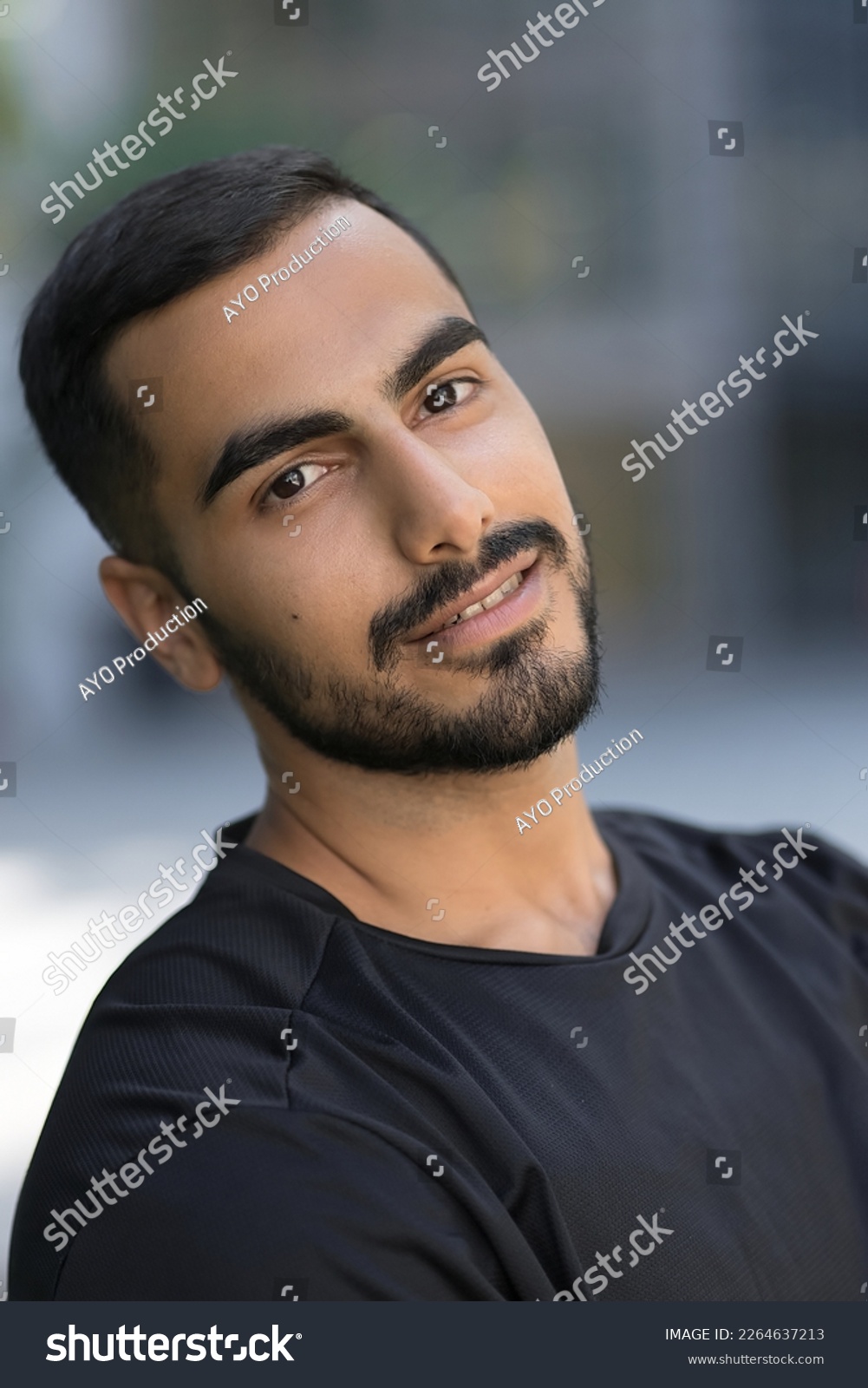 Smiling confident middle eastern man looking at camera on the street. Iranian hipster male with black hair wearing dark clothes standing outdoor  #2264637213