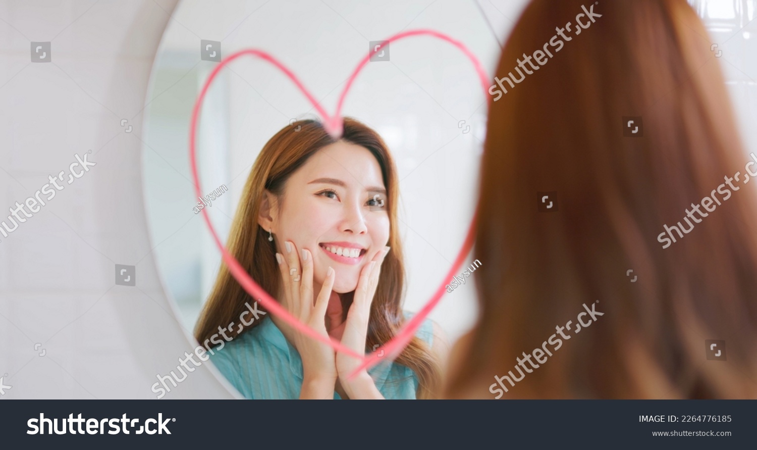 asian smiling beauty woman is looking in mirror which has big red heart shape sign and she touching her face #2264776185