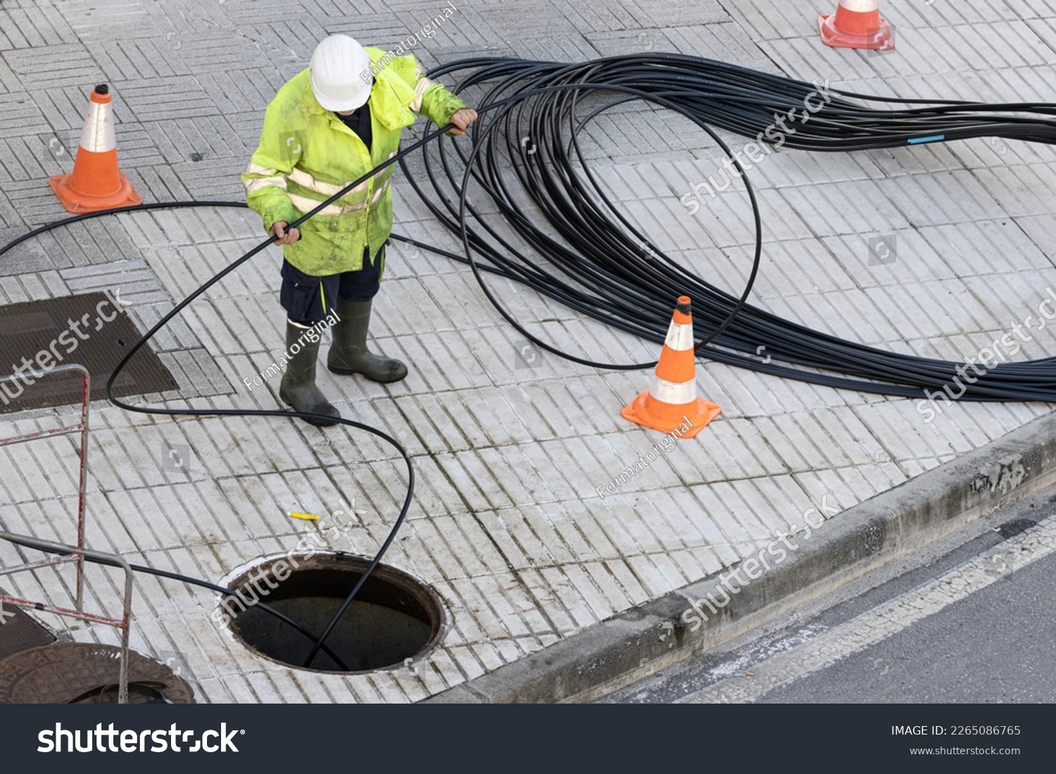 A worker is performing maintenance tasks on a communication cable located on the sidewalk of a city #2265086765