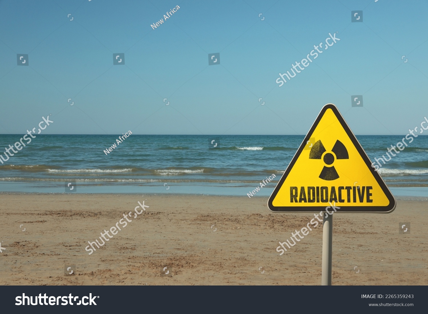 Radioactive pollution. Yellow warning sign with hazard symbol near contaminated area on beach. Space for text #2265359243