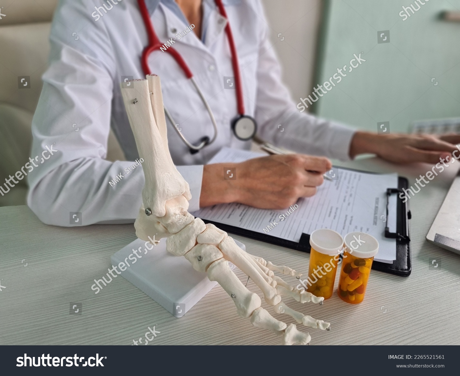 Doctor traumatologist writes out prescription for pills and leg skeleton. Pain in legs with osteoarthritis of bones and treatment with calcium and protein #2265521561