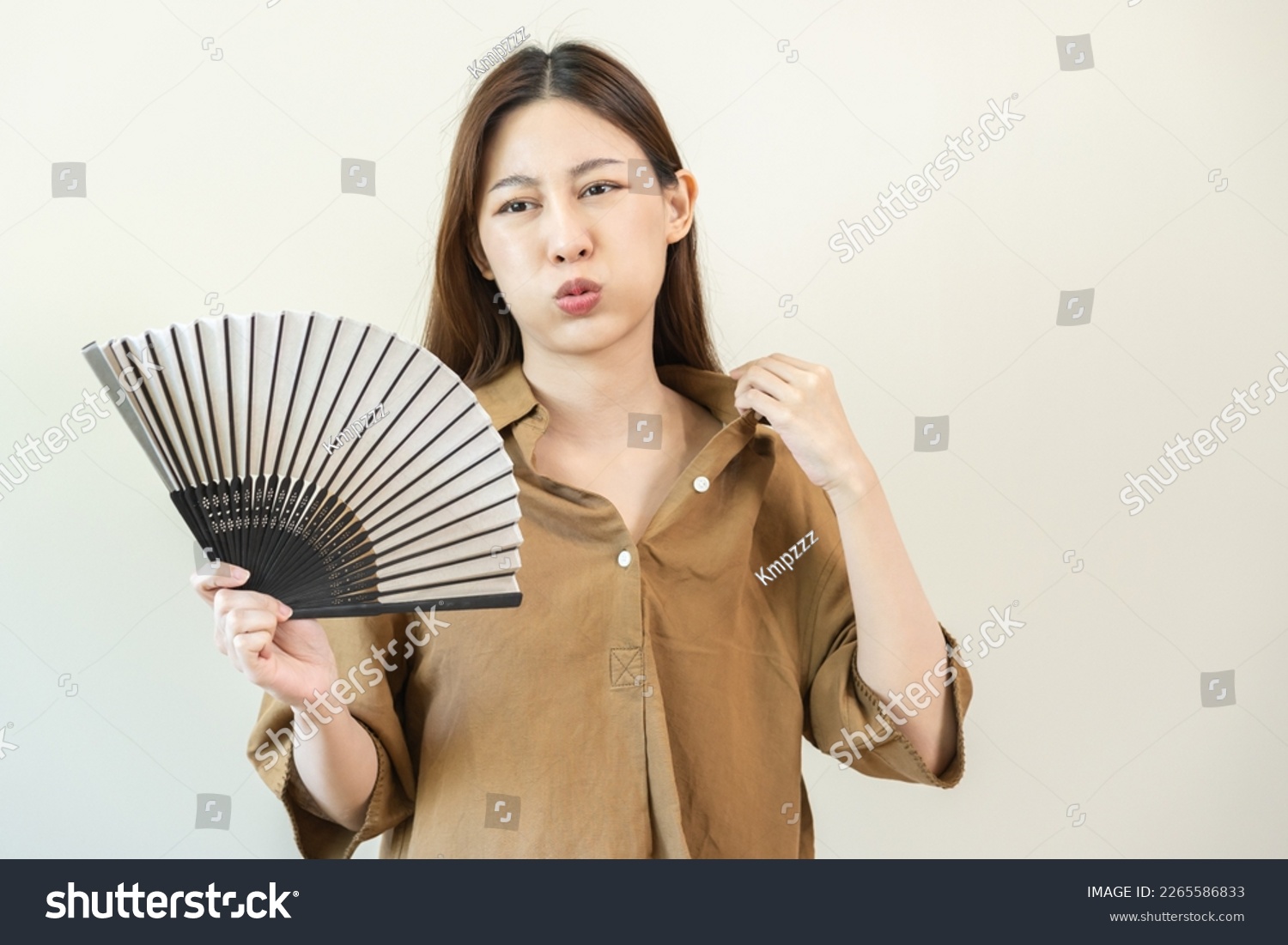 Suffering summer heat stroke, hot weather, tired asian young woman, girl sweaty and thirsty, refreshing with hand in blowing, wave fan to ventilation when temperature high at home, house on background #2265586833