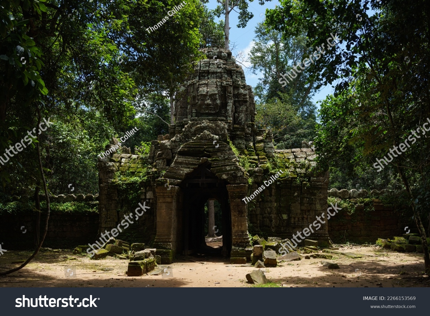 A photo of one of the gopuras at the Ta Som Temple site. It is constructed in the Bayon Style with a large carved stone face looking out from the top. Moss and foliage grow from the weathered stone. #2266153569