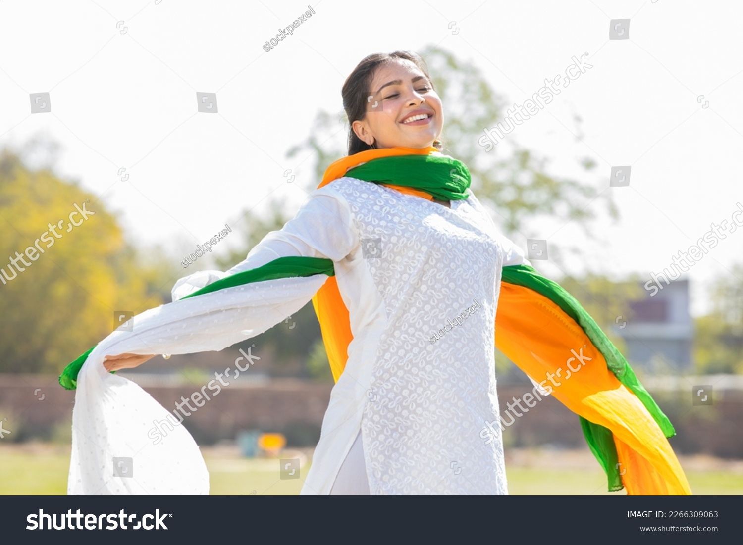 Portrait of happy young indian woman wearing traditional white kurta and tricolor duppata running at park. celebrating Independence day or Republic day. #2266309063