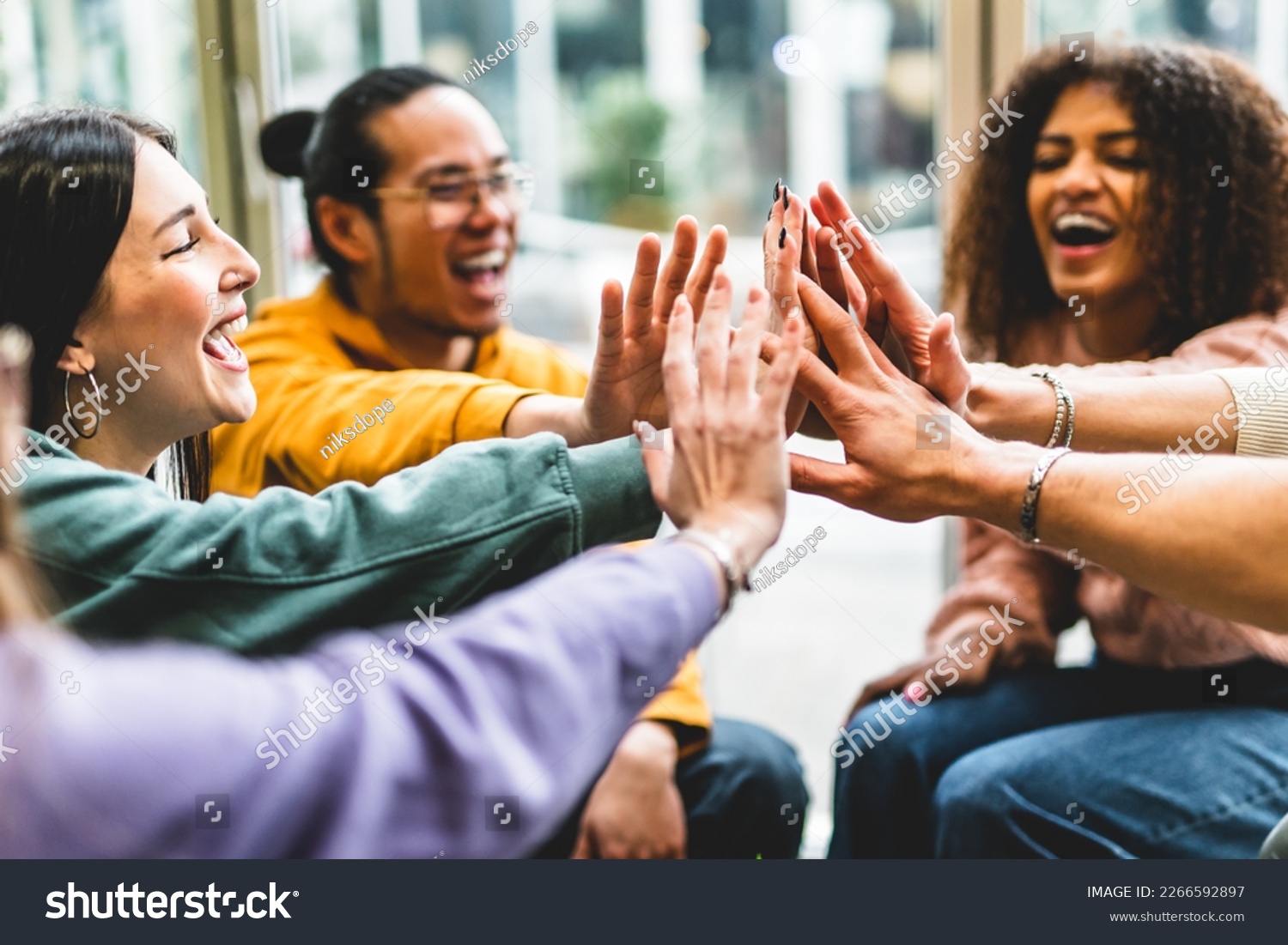 Multiracial happy young people stacking hands-Group of diverse friends having fun unity together indoors at table of community-Human resources Concept Creative and Relationship Youth Culture #2266592897