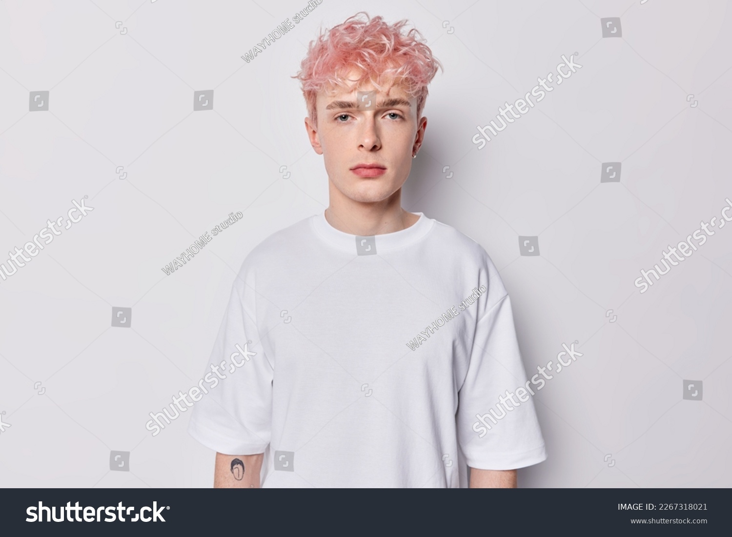 Portrait of attentive hipster guy with pink hair and tattoo on arm dressed in casual basic t shirt looks directly at camera has serious expression isolated over white background belong to subculture #2267318021