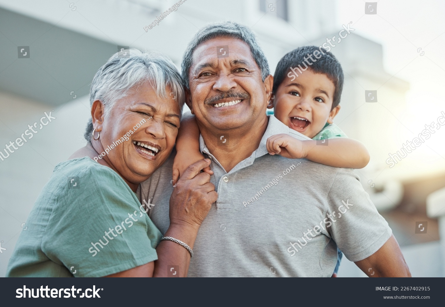 Grandparents, hug and child with smile for happy holiday or weekend break with elderly people at the house. Portrait of grandma and grandpa holding little boy on back for fun playful summer together #2267402915