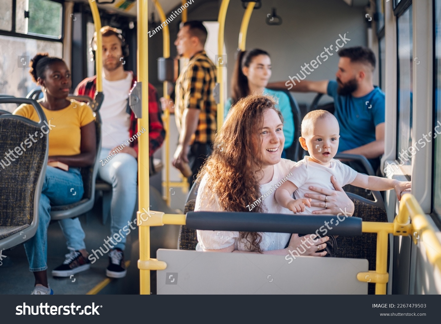 Young caring mother sitting with son in a bus while riding in a city. Boy is sitting in her lap and looking trough a window. Close up of plus size mom holding her child in public transportation. #2267479503