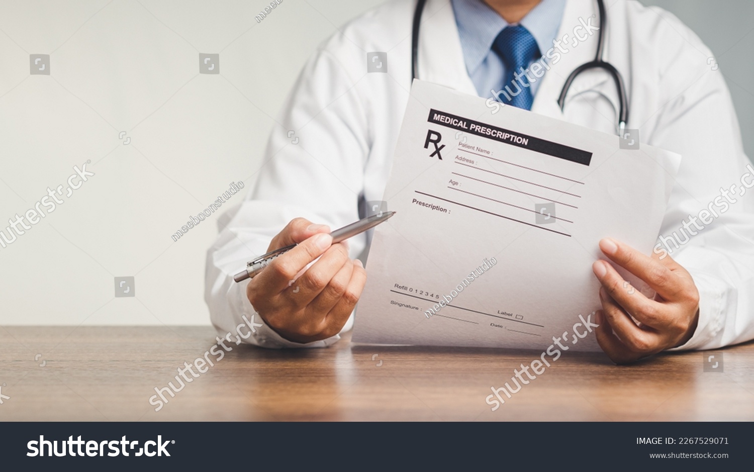 A doctor is holding a pen and a medical prescription while sitting in the hospital. Medical personnel, medicine, and science concept. Quality medical services #2267529071