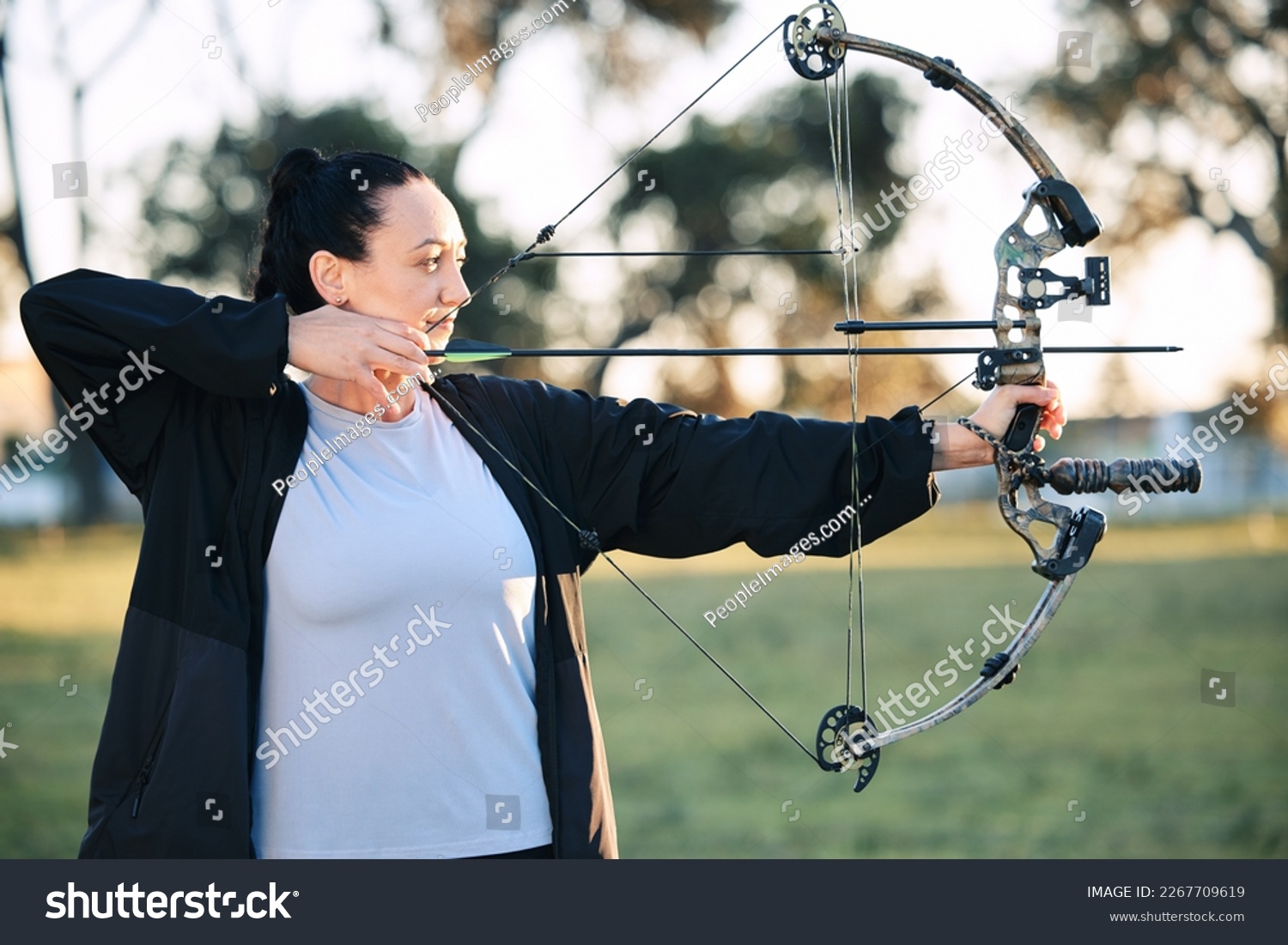Hobby, learning and woman playing archery as a sport, outdoor activity and game in nature of France. Training, practice and girl with a bow and arrow for sports, competition and shooting at a park #2267709619