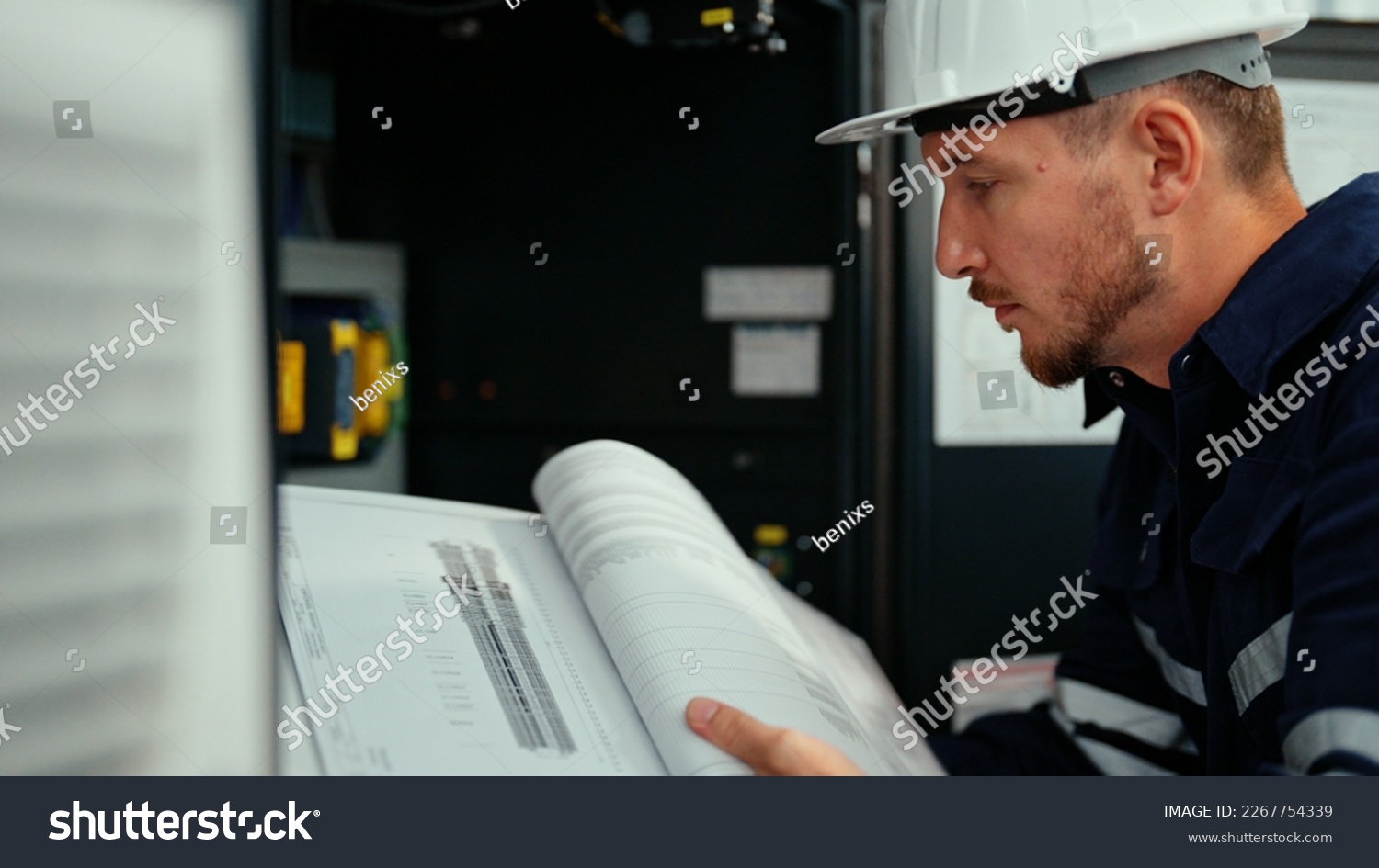 Caucasian production engineer in safety wear is reading the manual of a machine to find an error. A male factory worker is checking the industrial control panel of a robotic machine for maintenance. #2267754339
