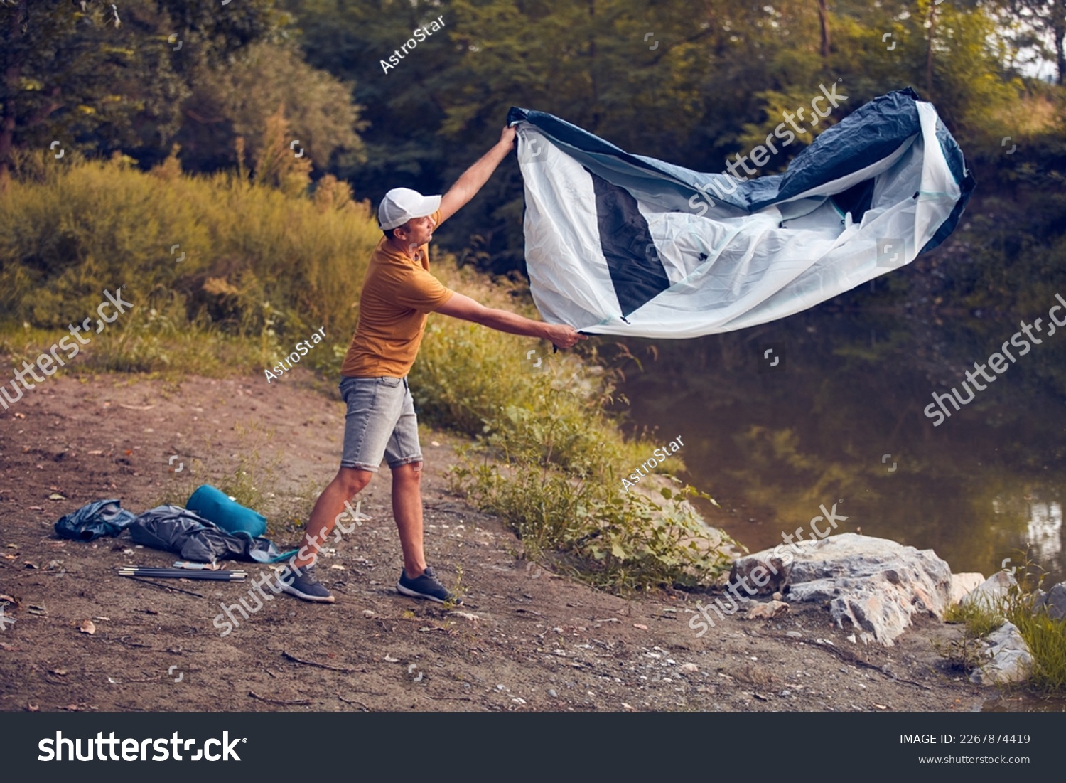 Man camping in nature, setting up the tent for overnight staying near forest river. #2267874419