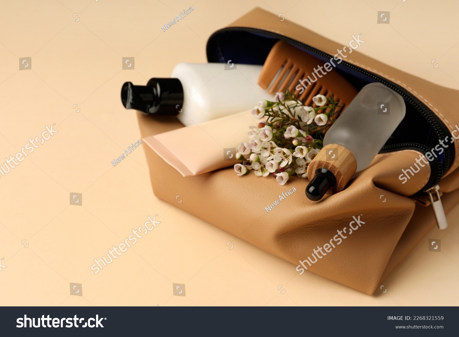 Preparation for spa. Compact toiletry bag with different cosmetic products and flowers on beige background, closeup. Space for text #2268321559