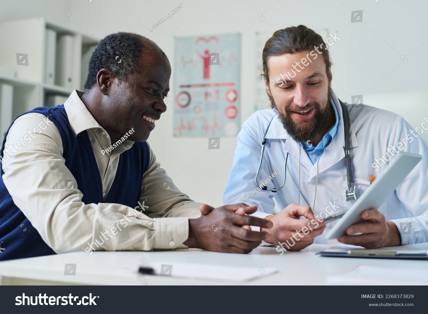 Young smiling doctor pointing at tablet screen with results of medical test and explaining diagnosis to senior African American male patient #2268373829