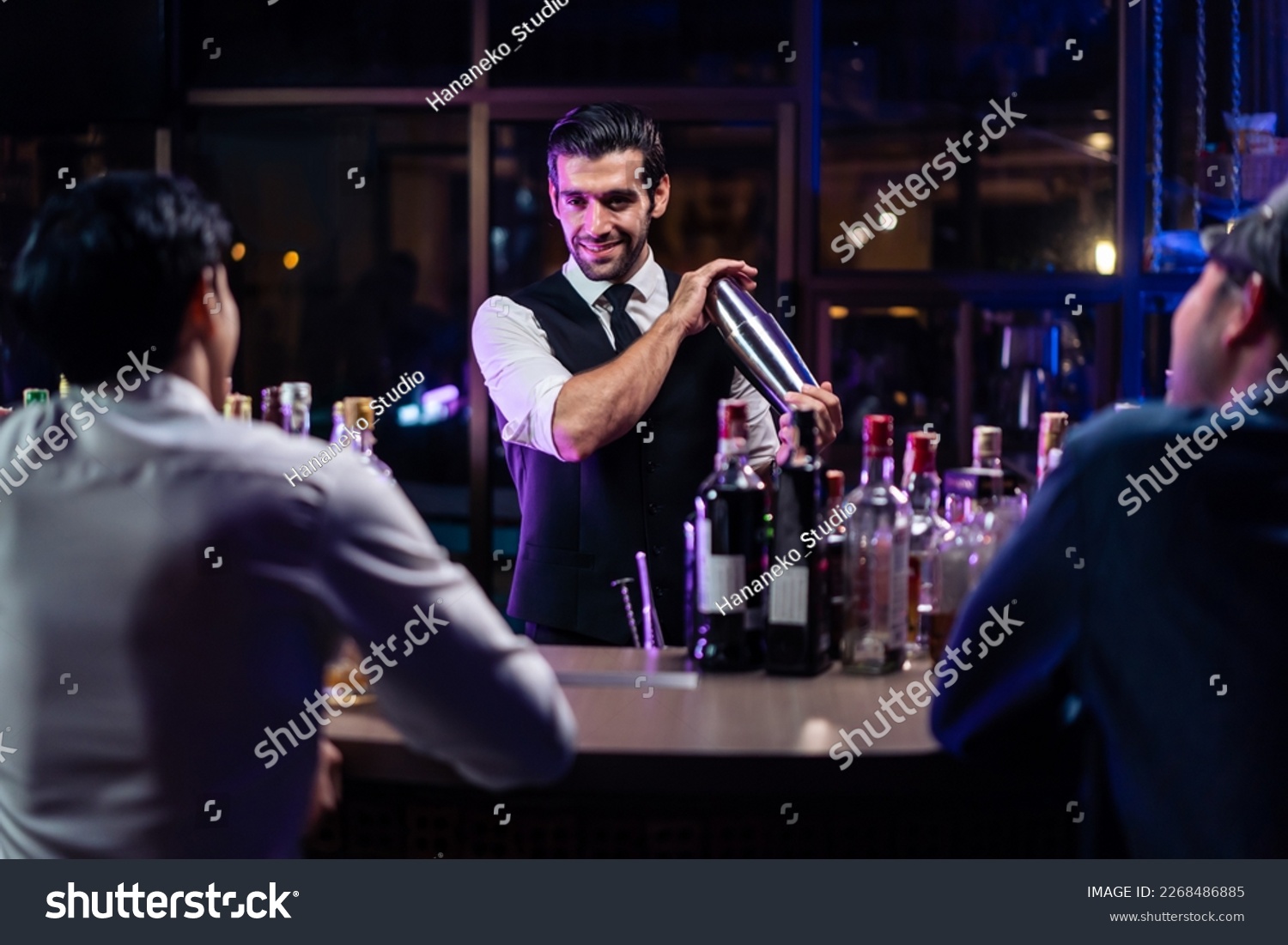 Caucasian profession bartender making a cocktail for women at a bar. Attractive barman pouring mixes liquor ingredients cocktail drink from cocktail shaker into the glass at night club restaurant. #2268486885