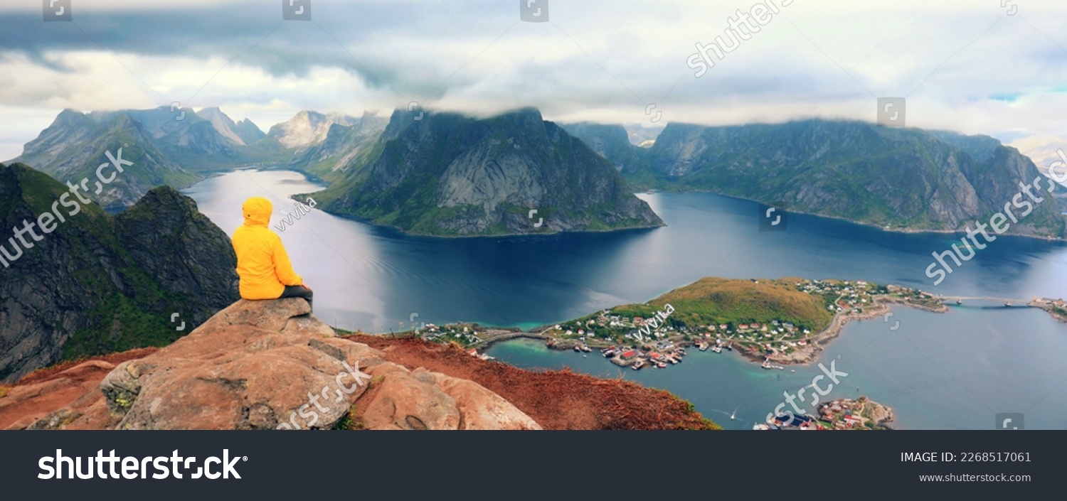 Solitude with nature. Panoramic aerial view of fjord and fishing village. Man tourist sitting on a cliff of rock. Beautiful mountain landscape. Nature Norway, Lofoten islands.  #UniqueSSelf #2268517061
