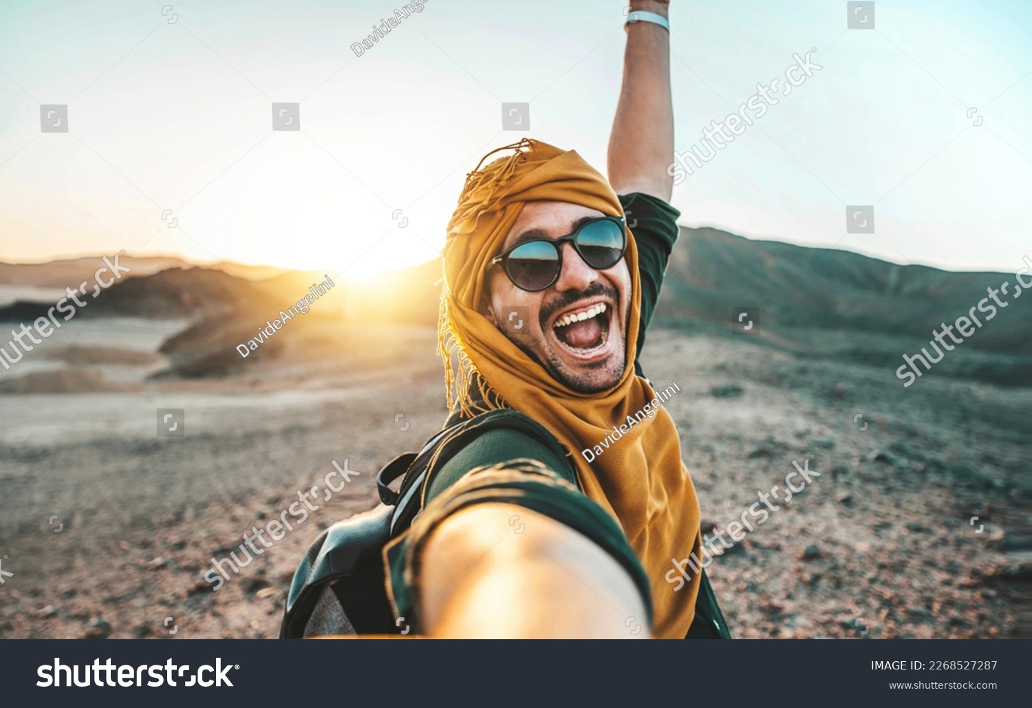 Handsome man taking selfie pic with smart mobile phone outside at golden hour time - Traveler guy with backpack enjoying day out on summer vacation - Happy tourist having fun at summertime holiday #2268527287