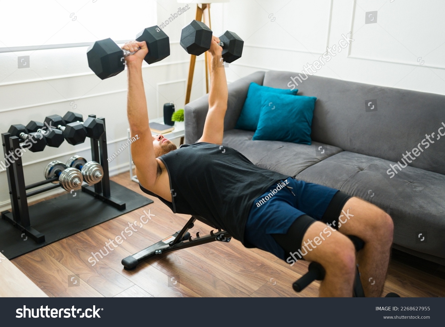 Strong fit man in his 20s with a home gym doing bench press exercises with dumbbell weights #2268627955