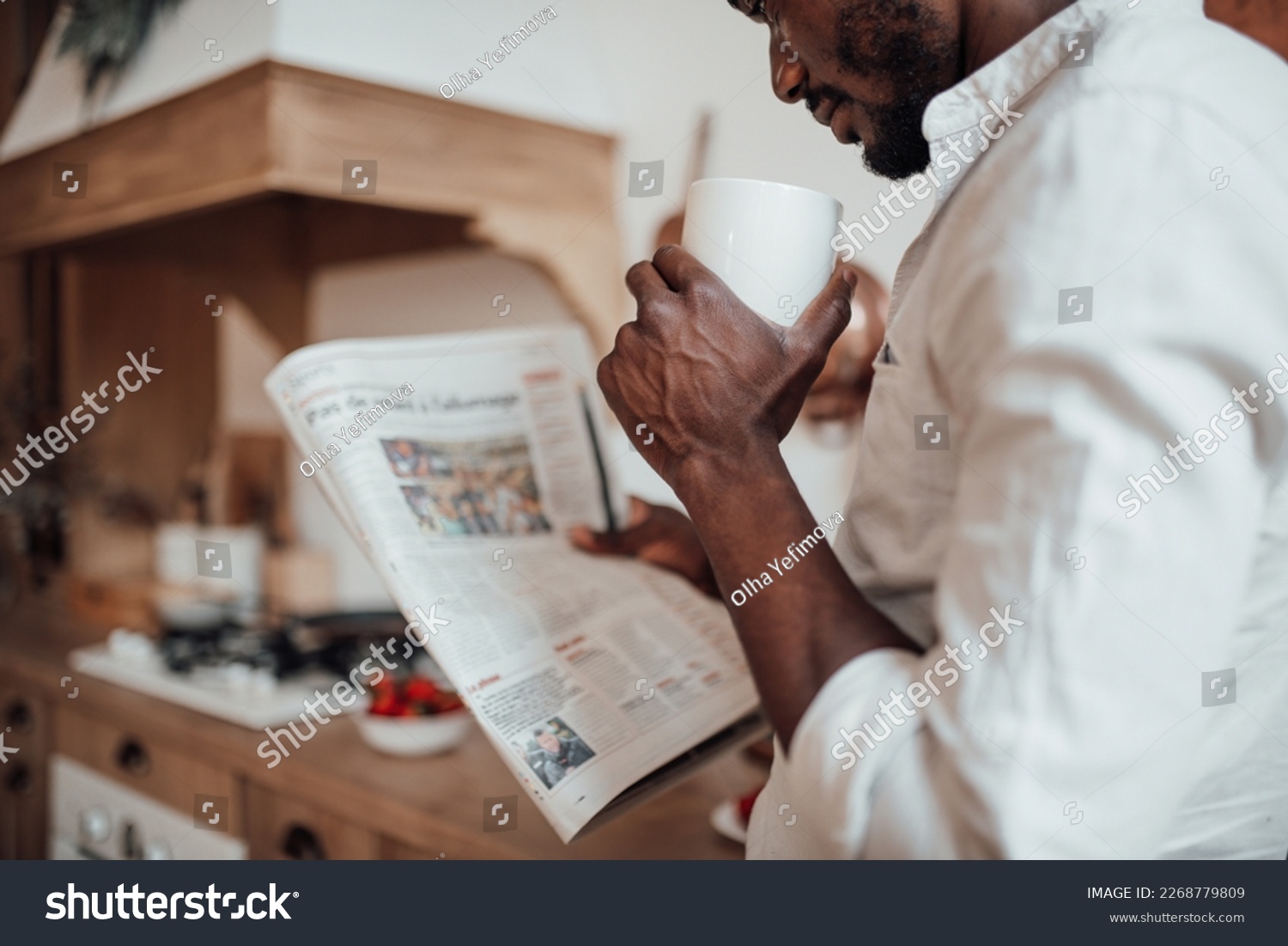 Candid millennial authentic diverse portrait of african american man relax time in neutrals tones kitchen. Brown skin male drink tea at breakfast domestic life and morning routine reading newspaper #2268779809