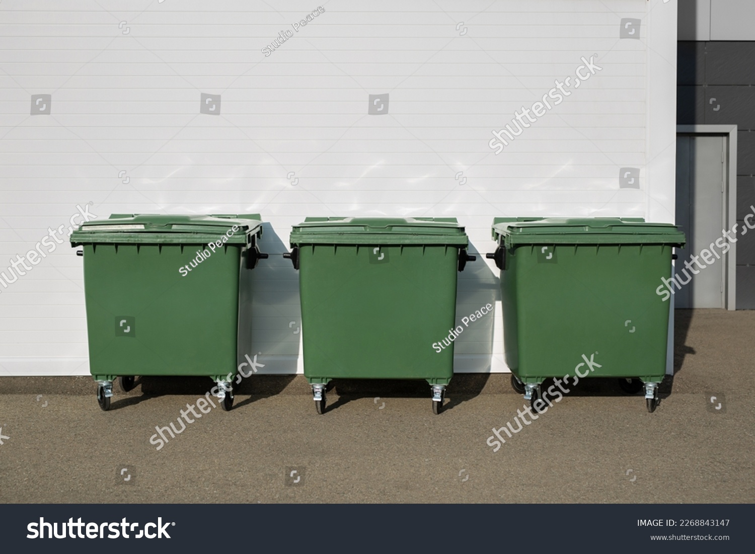 Three green dumpsters on the street. Garbage bin #2268843147