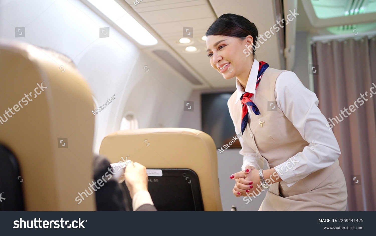Friendly Asian female flight attendant serving food drink and talking to passengers on airplane. Airline service #2269441425