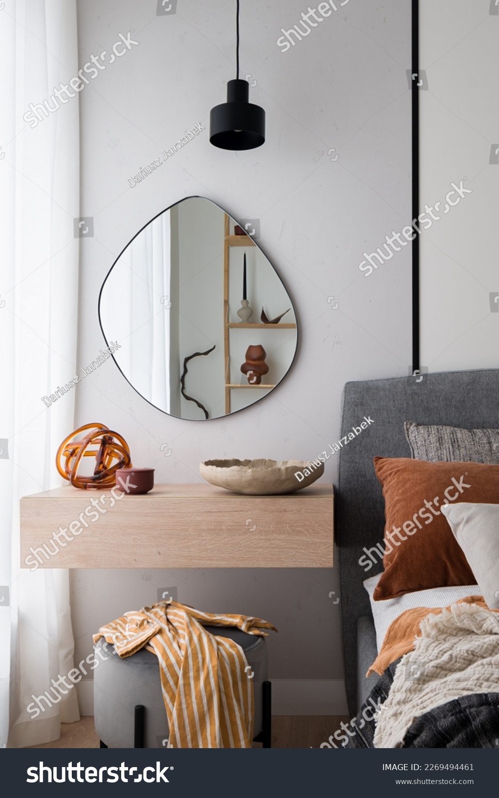 Modern, irregular shaped mirror above simple, wooden dressing table next to cozy bed in bedroom #2269494461