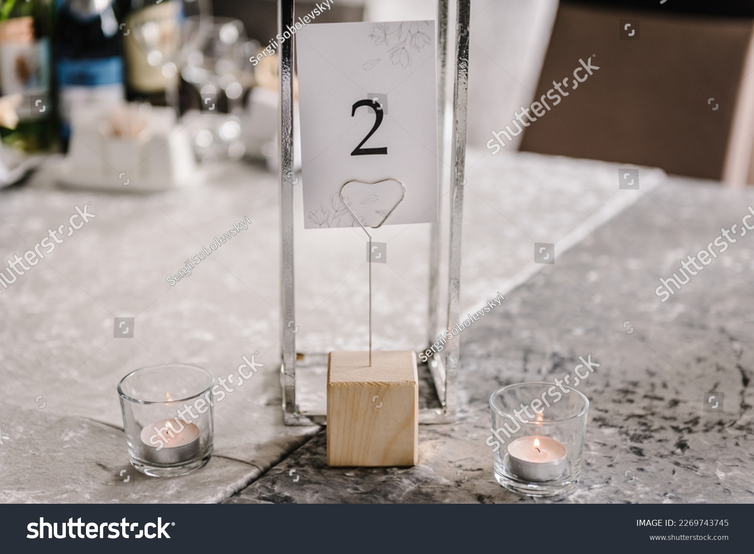 Table number 2. Setting, serving guests closeup. Stands, sign number two. Close up. Wedding setup detail. Festive table covered tablecloth, decorated composition flowers and candles in party area #2269743745