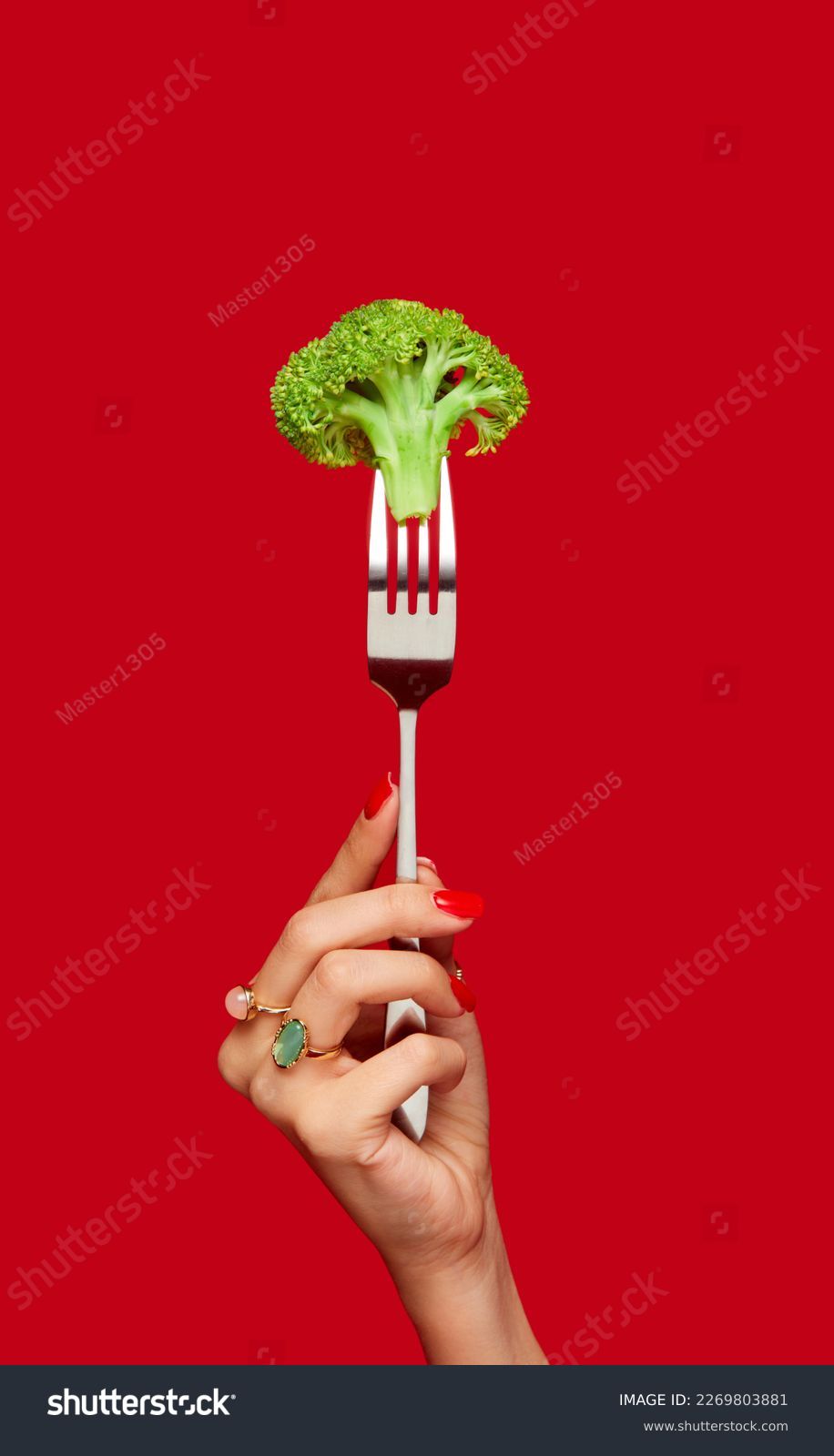 Female hand holding broccoli on fork against red studio background. Healthy eating. Food pop art photography. Concept of art and creativity. Complementary colors. Copy space for ad, text #2269803881