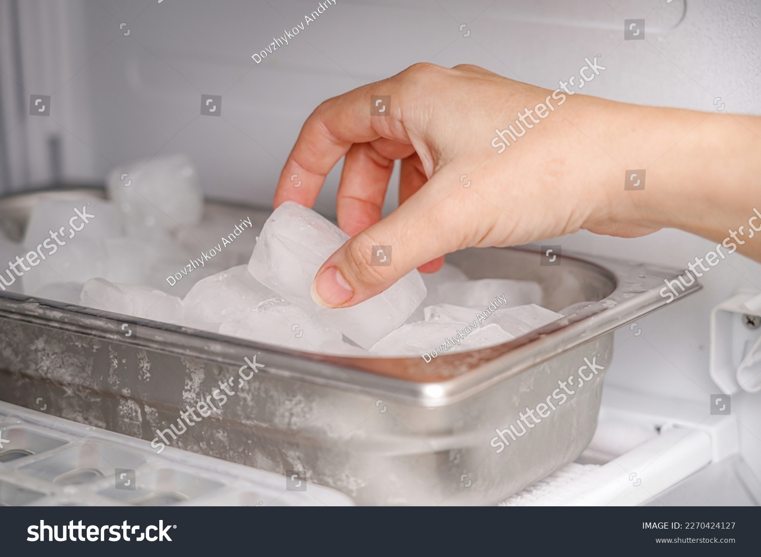 The girl takes frozen ice cubes from the freezer with her hand to prepare soft drinks. #2270424127