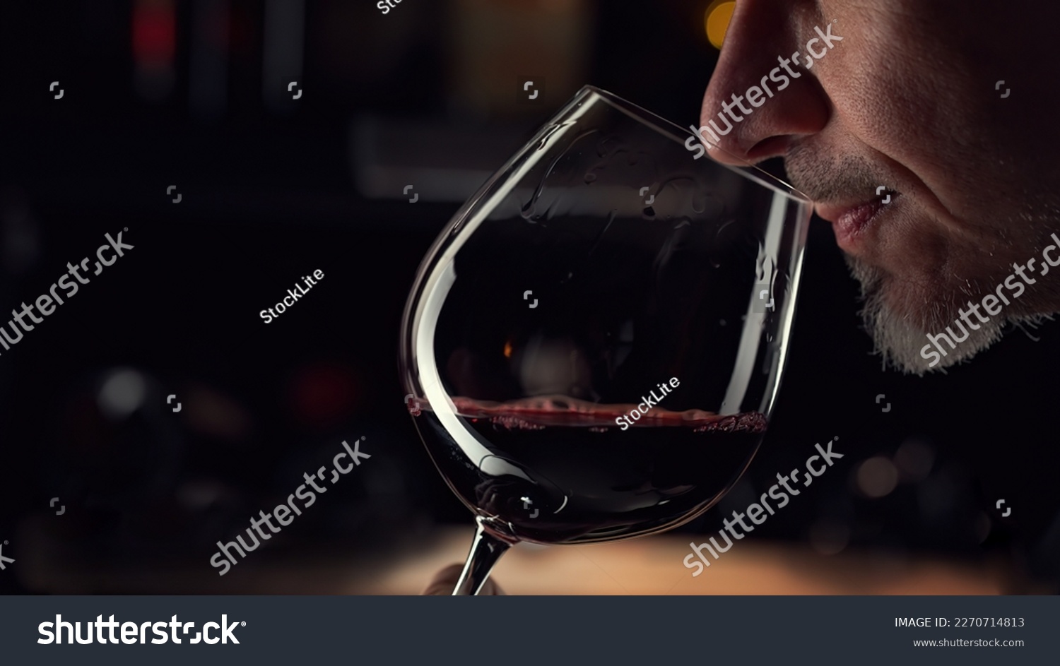 Close up man smelling red wine in wine glass. Wine expert tasting, rating and drinking wine, bottles in background. #2270714813