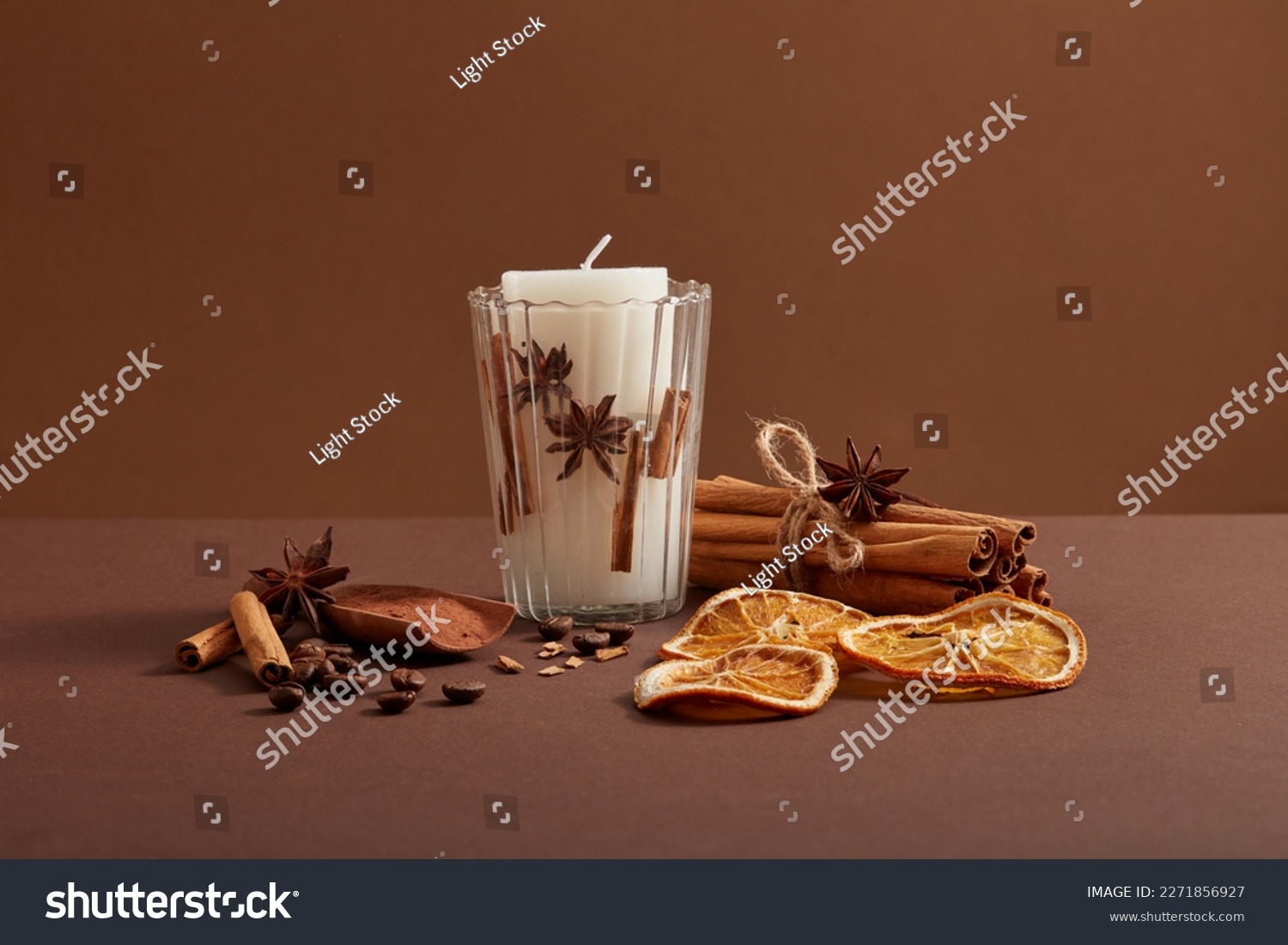 A white candle putted on a transparent glass and a bunch of cinnamon sticks, coffee beans, star anise and dried orange slices decorated around. #2271856927