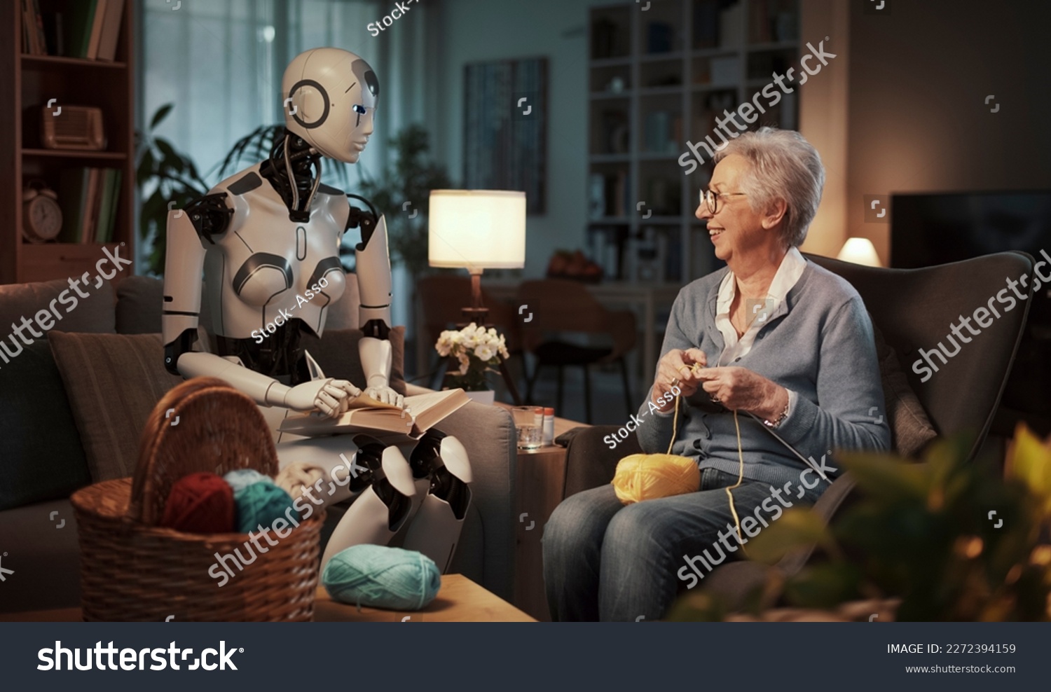 Elderly woman knitting on a sofa with her companion android reading a book in the living room. Concept of elderly care and future. #2272394159