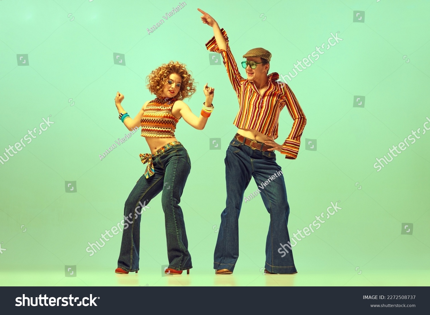 Happy and active dancers. Two excited people, man and woman in retro style clothes dancing disco dance over green background. 1970s, 1980s fashion, music, hippie lifestyle #2272508737